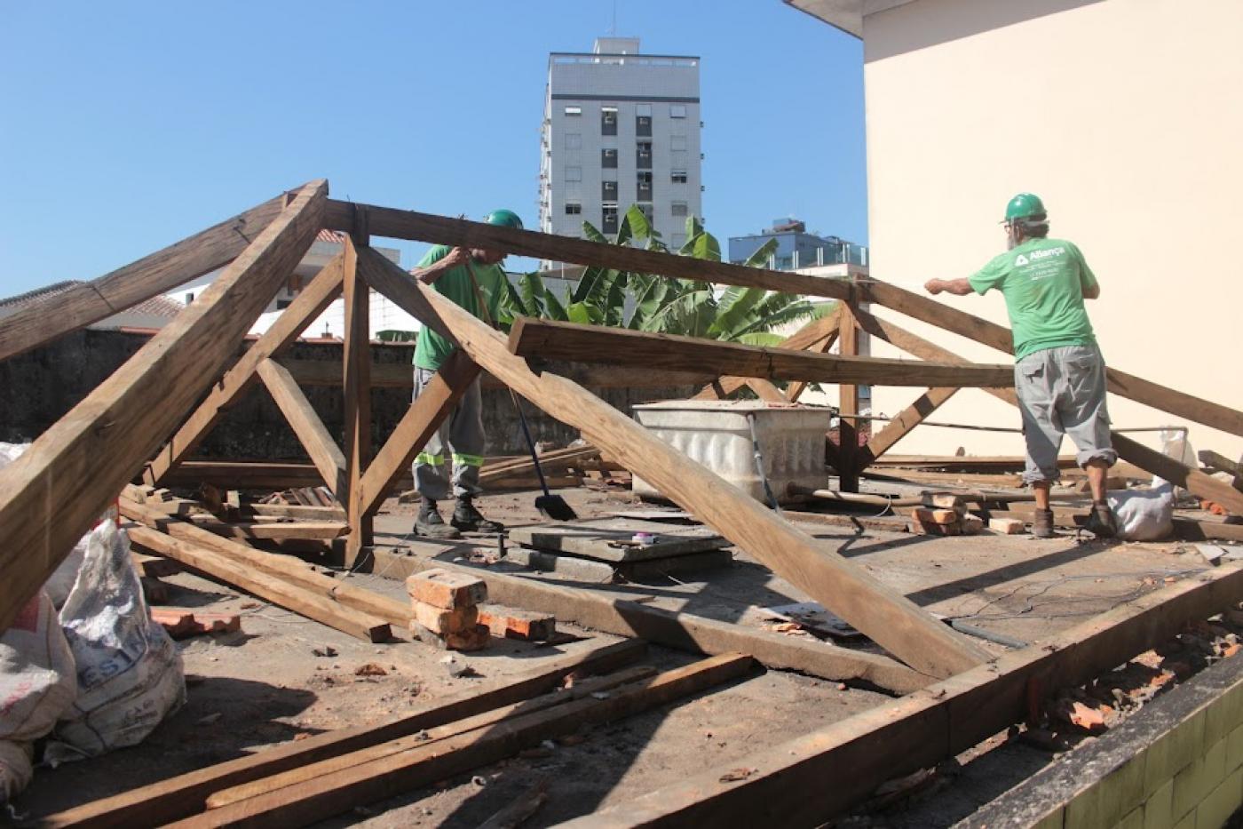 dois homens estão trabalhando em telhada com estrutura de telhas em madeira aparente. #paratodosverem