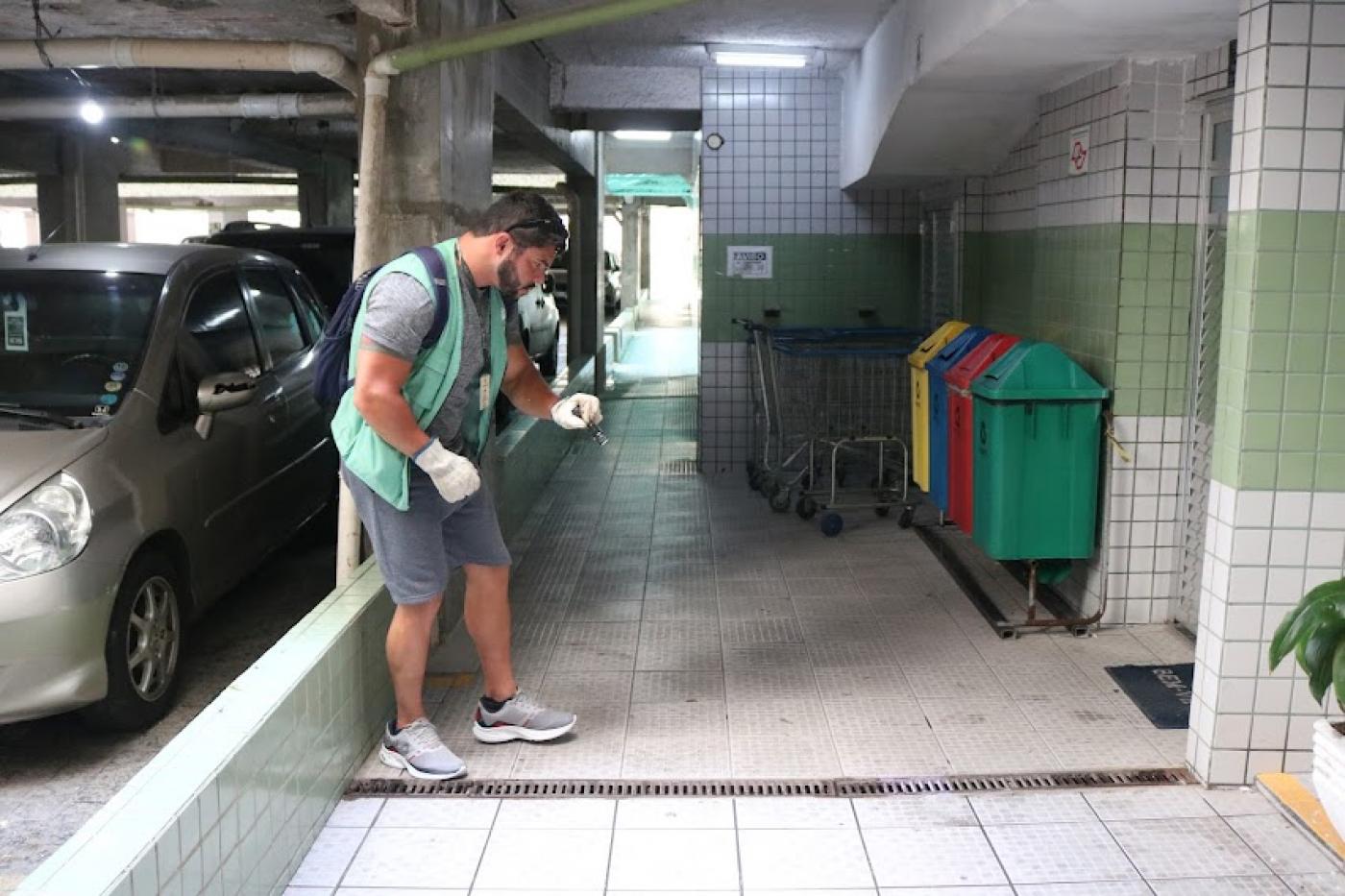 agente está em pé em garagem iluminando ralo com lanterna. #paratodosverem