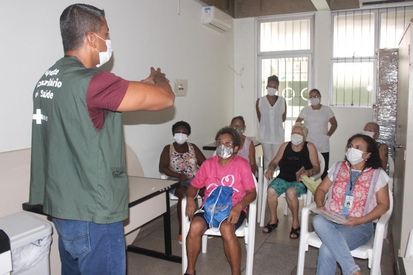 agente de saúde está em pé falando a mulheres que estão sentadas. #paratodosverem