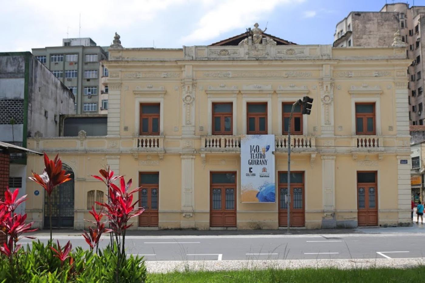 a fachada do teatro coliseu, com flores em uma praça (à esq.) em primeiro plano. #paratodosverem 
