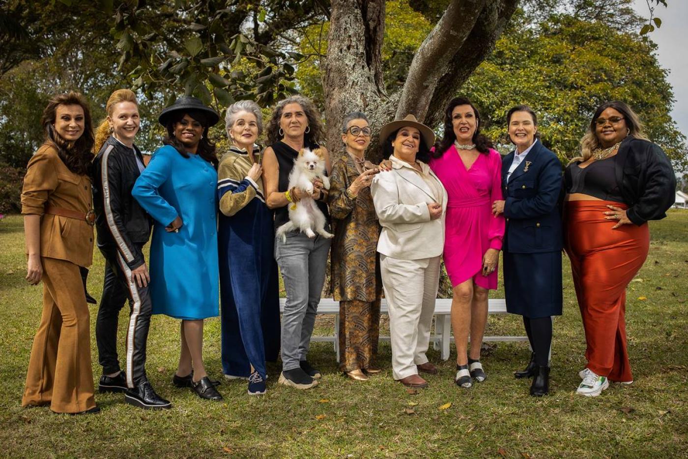 10 mulheres posam para foto em um gramado diante de uma árvore. Uma delas segura um cachorrinho no colo. #paratodosverem 
