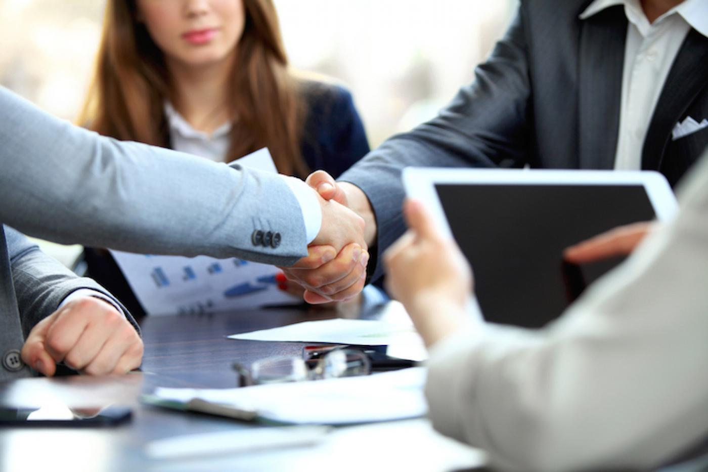 Pessoas apertam a mão sentados numa mesa #paratodosverem