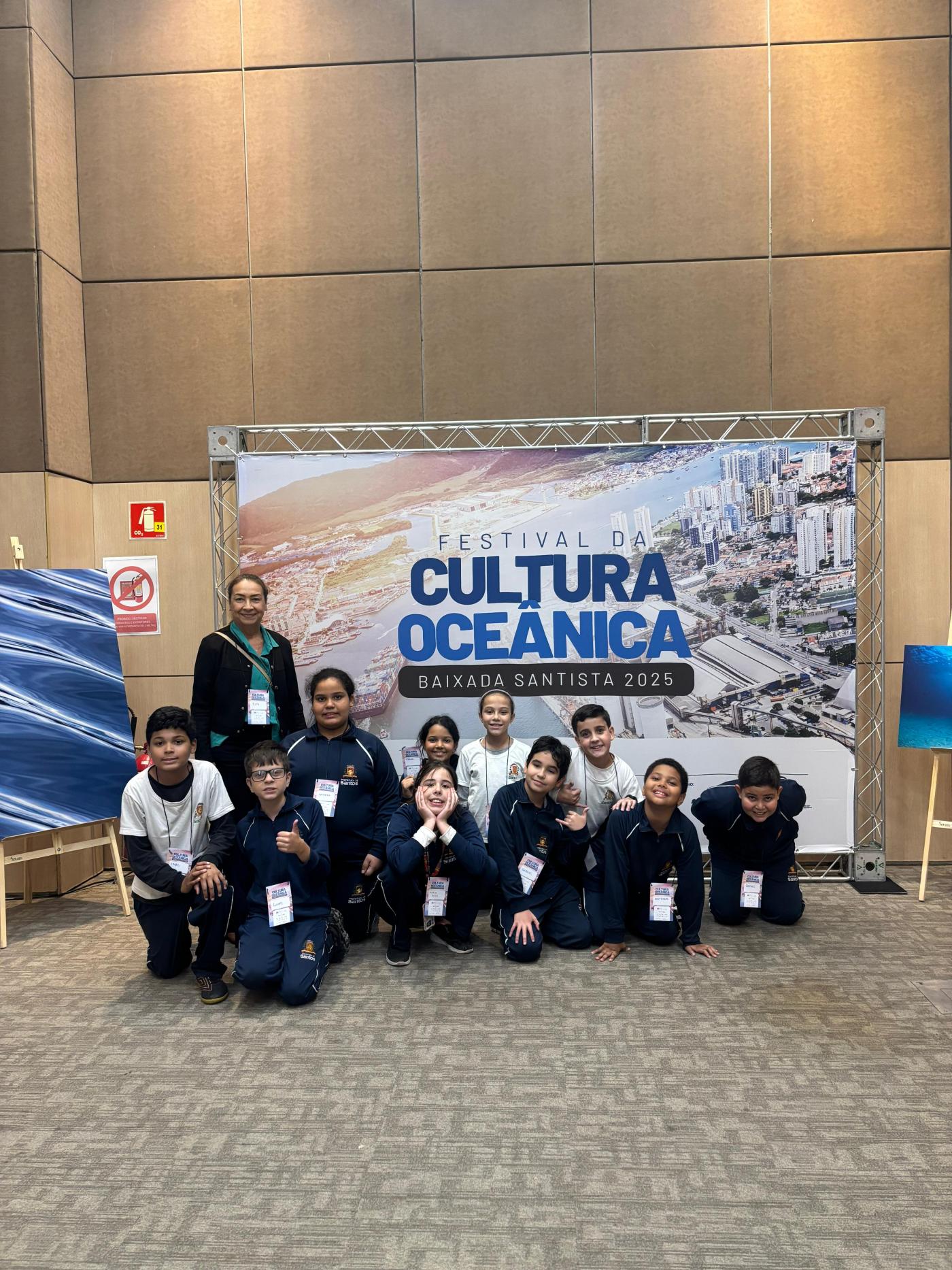 alunos posam na frente de placa do festival #paratodosverem