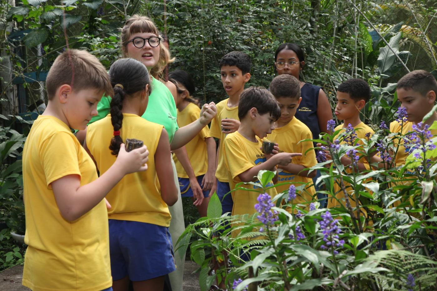 mulher orienta crianças em jardim florido. #paratodosverem