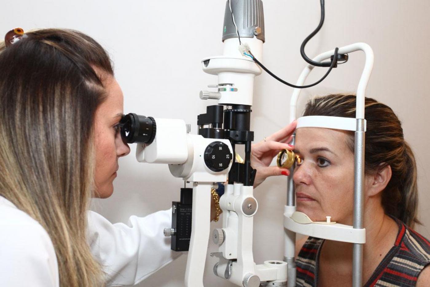 Médica está examinando olho de mulher com um aparelho. #paratodosverem