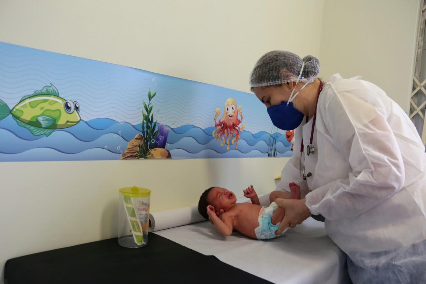médica está examinando bebê sobre maca. #paratodosverem