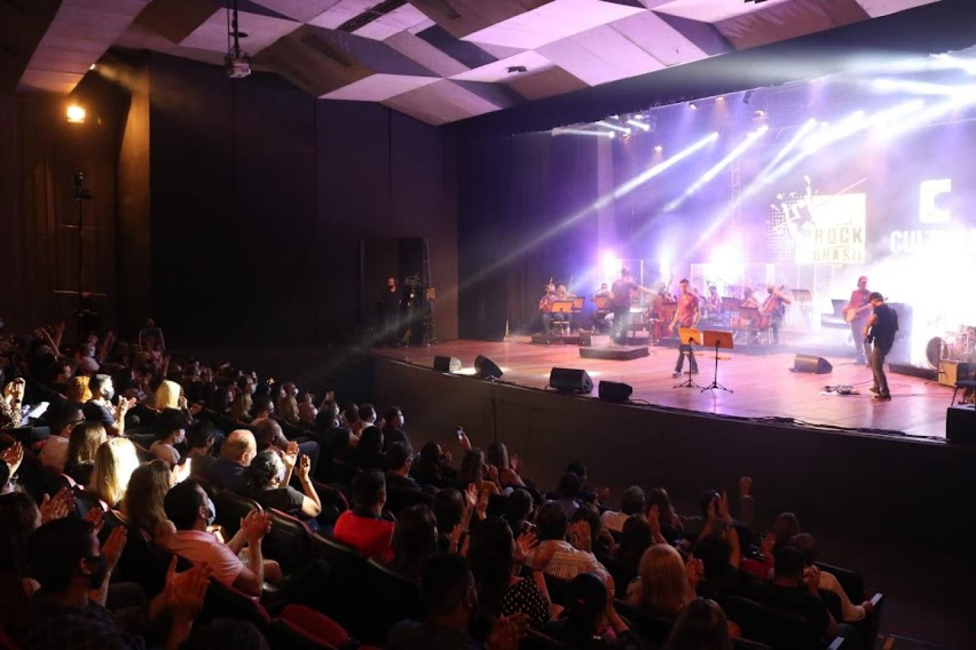 Público sentado aplaude músicos no palco #paratodosverem