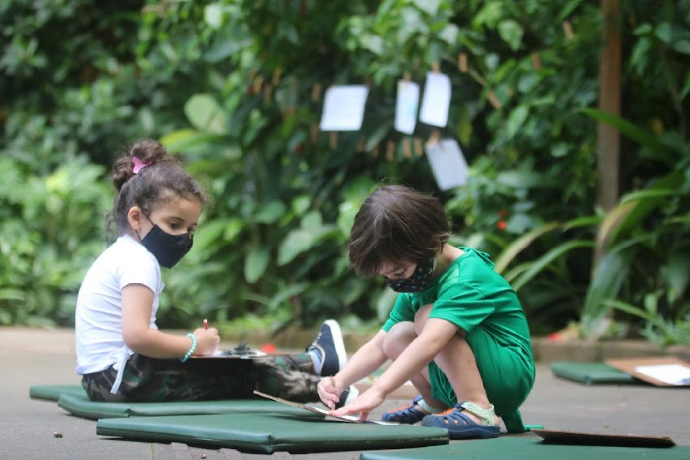 duas crianças brincam sentadas no chão do parque #paratodosverem