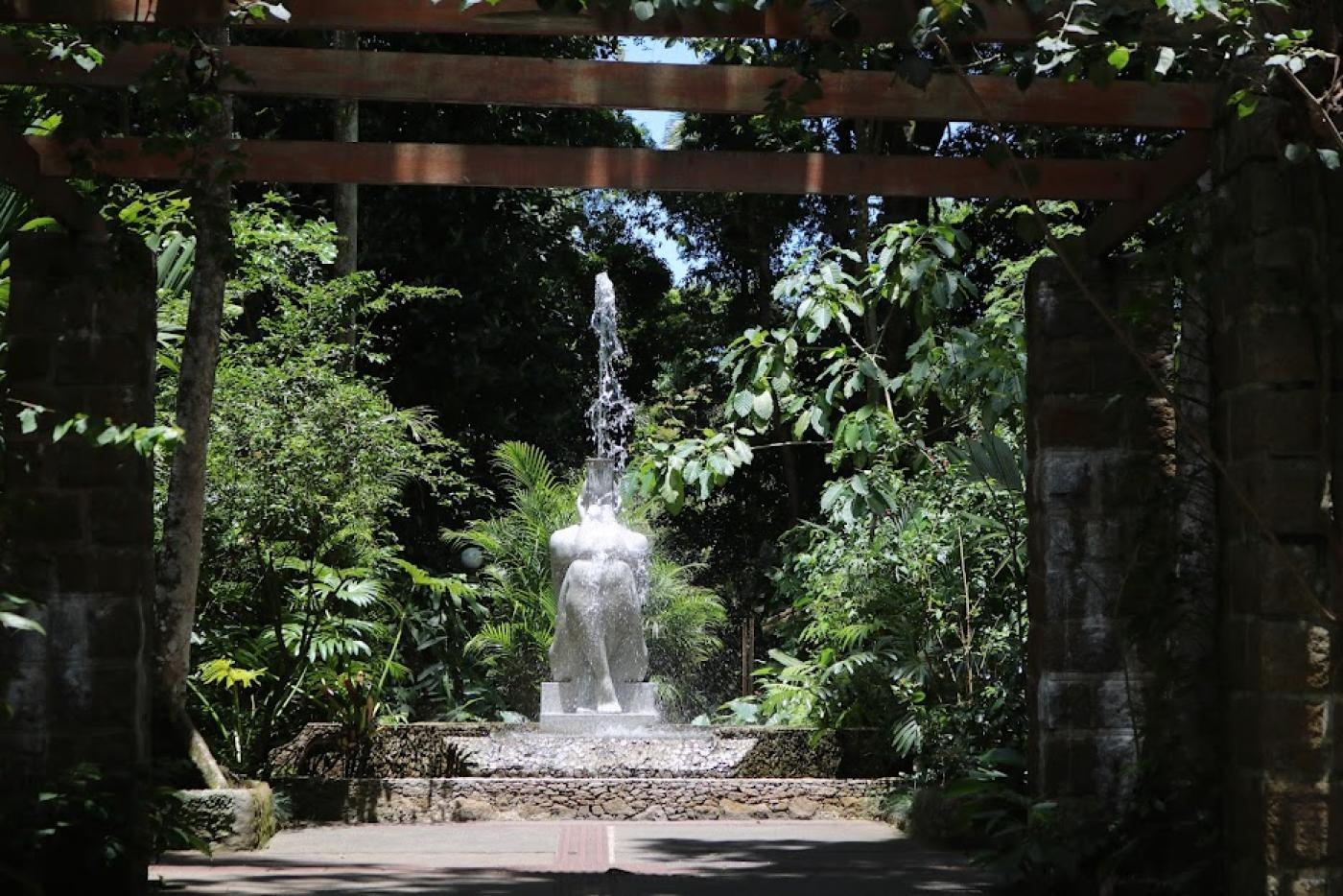 a entrada do orquidário, com vegetação nas laterais e a estátua da ninfa náiade ao centro e ao fundo. #paratodosverem