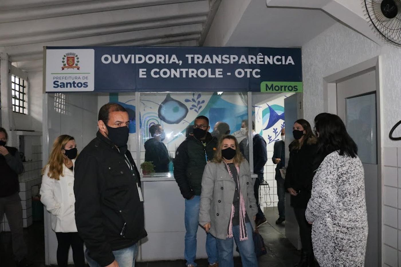 Cabine da ouvidoria com várias pessoas na frente. #paratodosverem