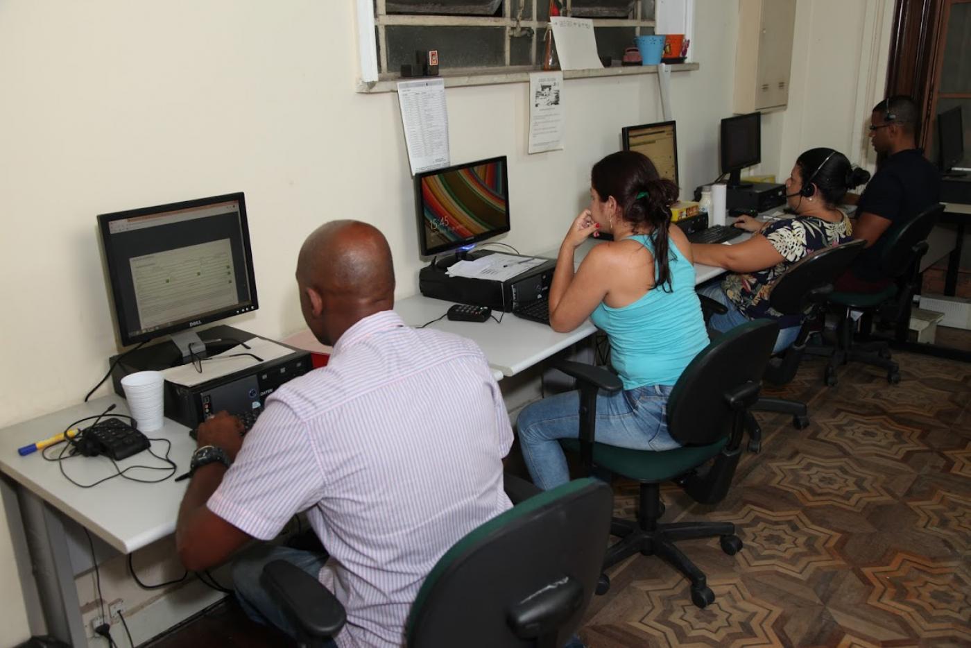 Agentes da ouvidoria sentados e de frente para tela de computador. #Paratodosverem