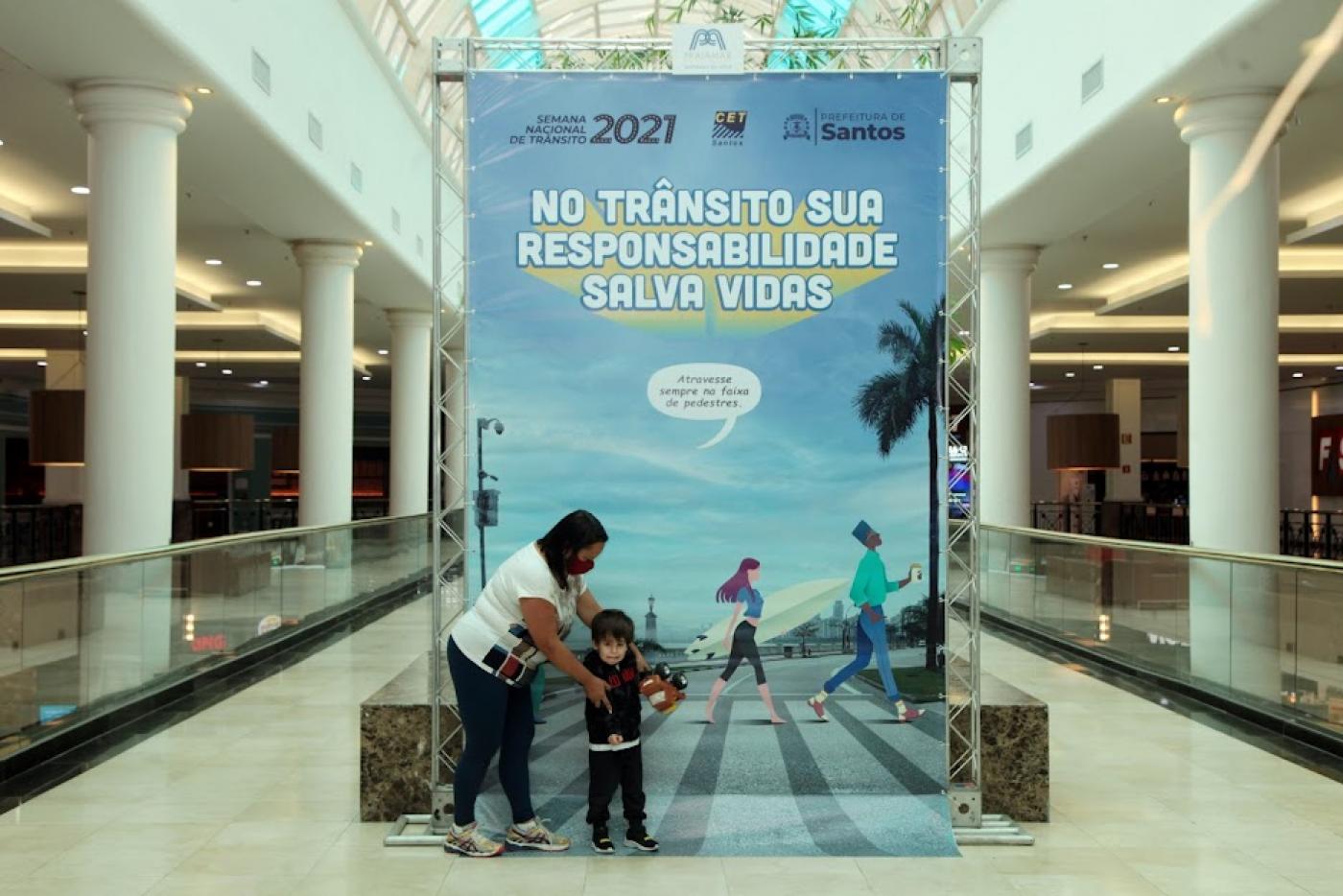 grande painel instagramável ao fundo. Mãe coloca filho pequeno na frente do painel. #paratodosverem