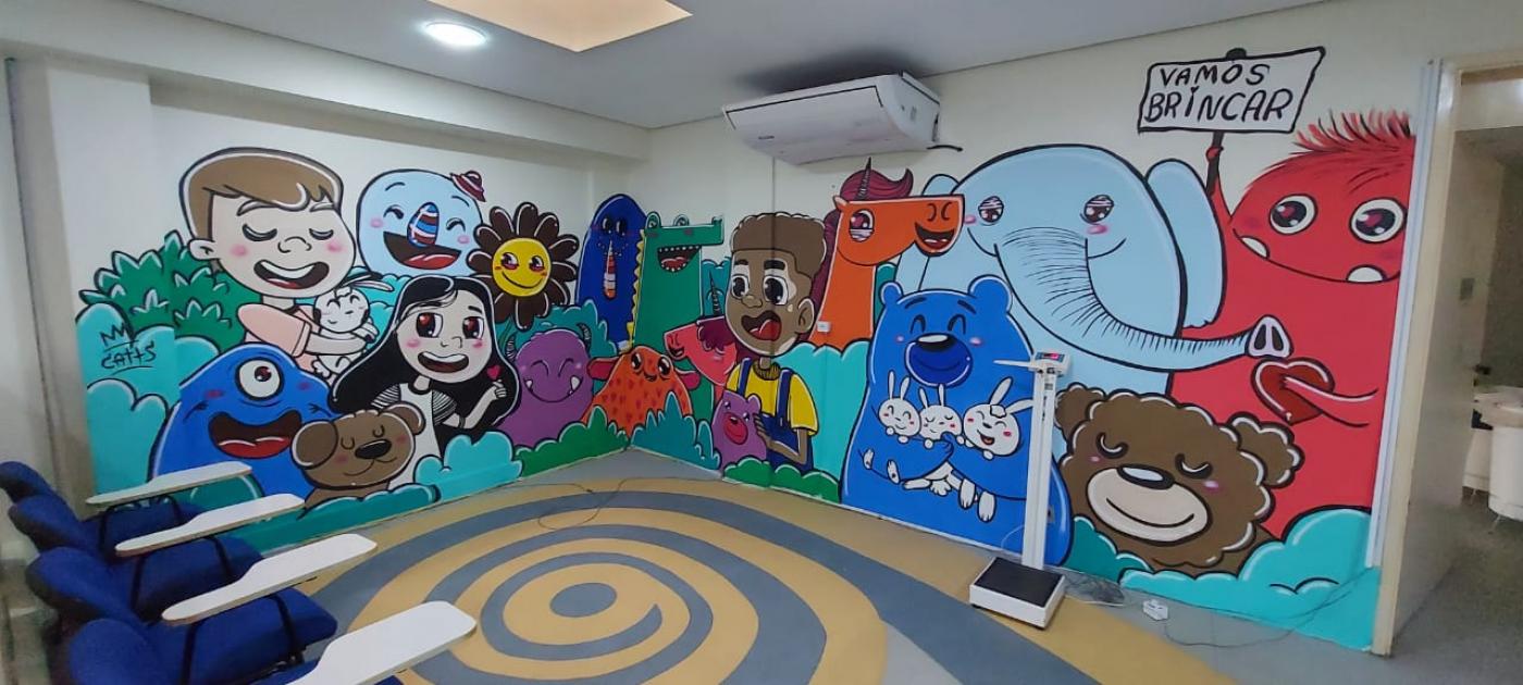 parede de hospital grafitada com imagens de crianças e animais coloridos. Um deles segura uma placa onde se lê 