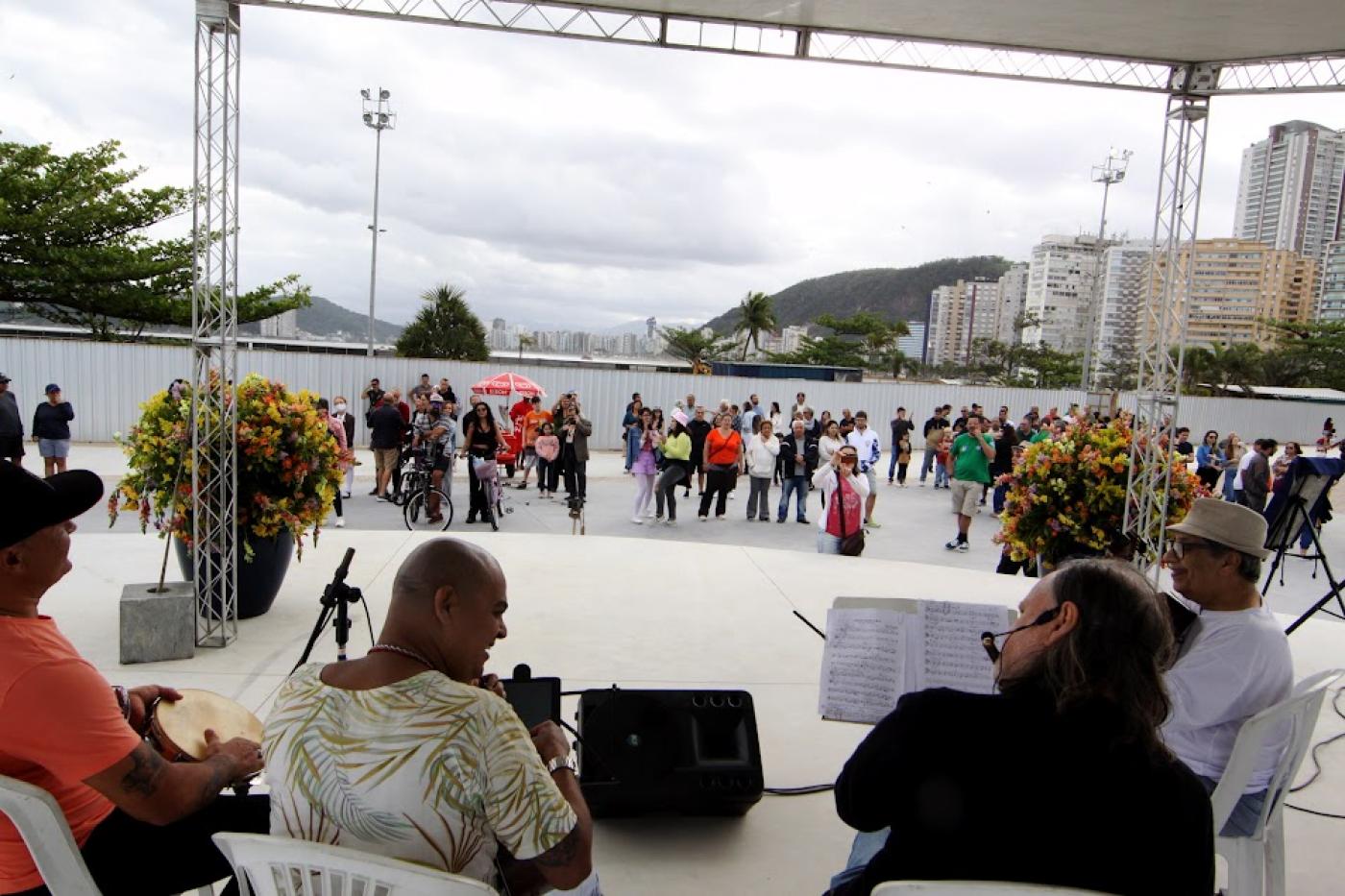 músicos tocam em palco e público está ao fundo. #paratodosverem