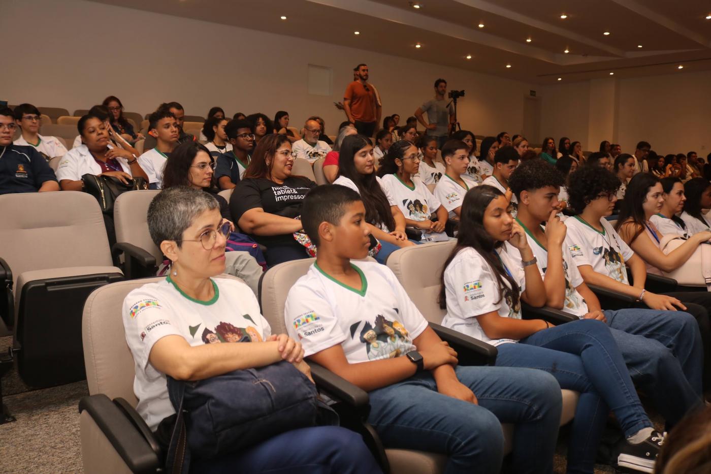 alunos uniformizados sentados em auditório. #paratodosverem 