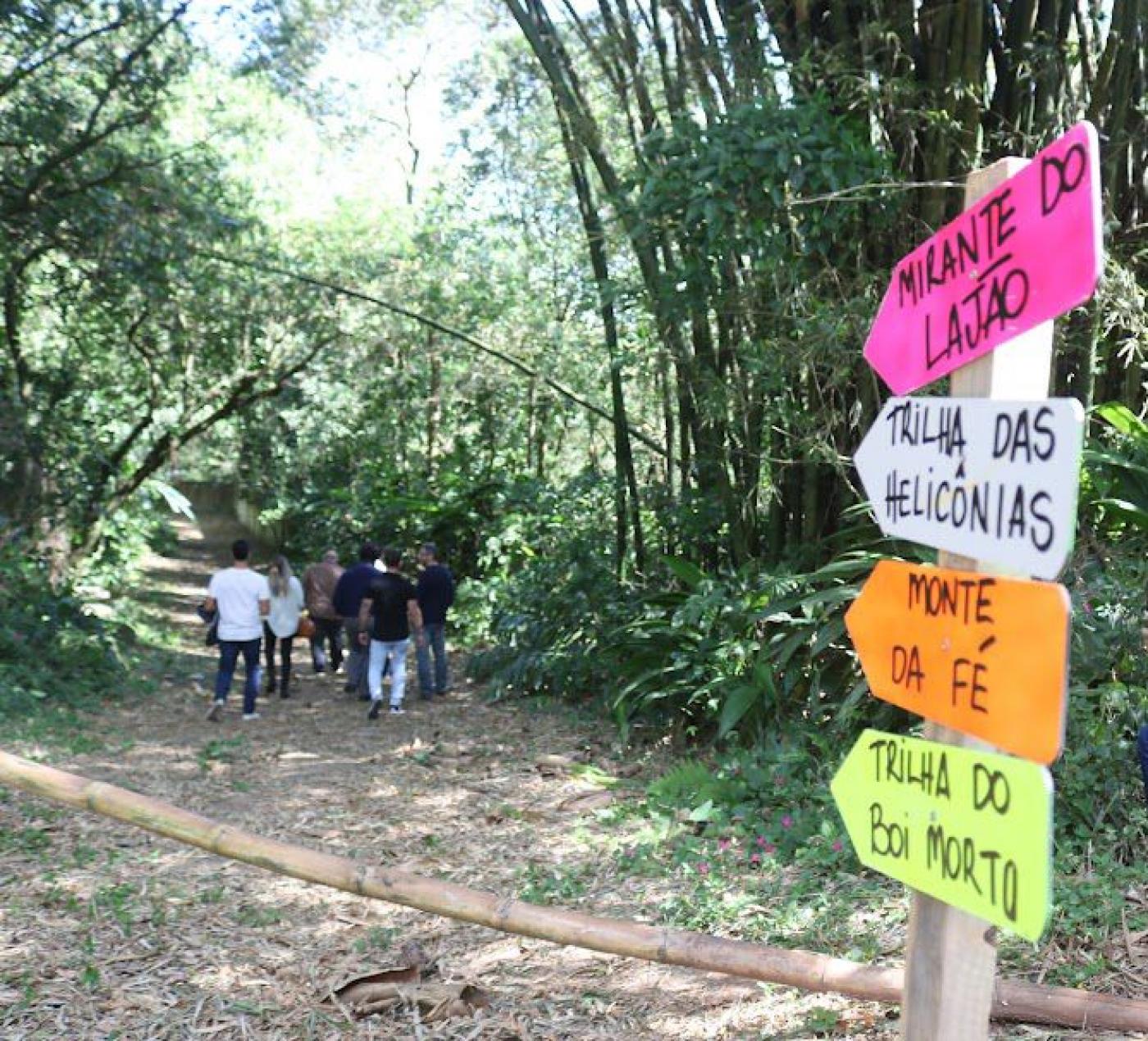 pessoas caminham por trilha sinalizada por placas. #paratodosverem