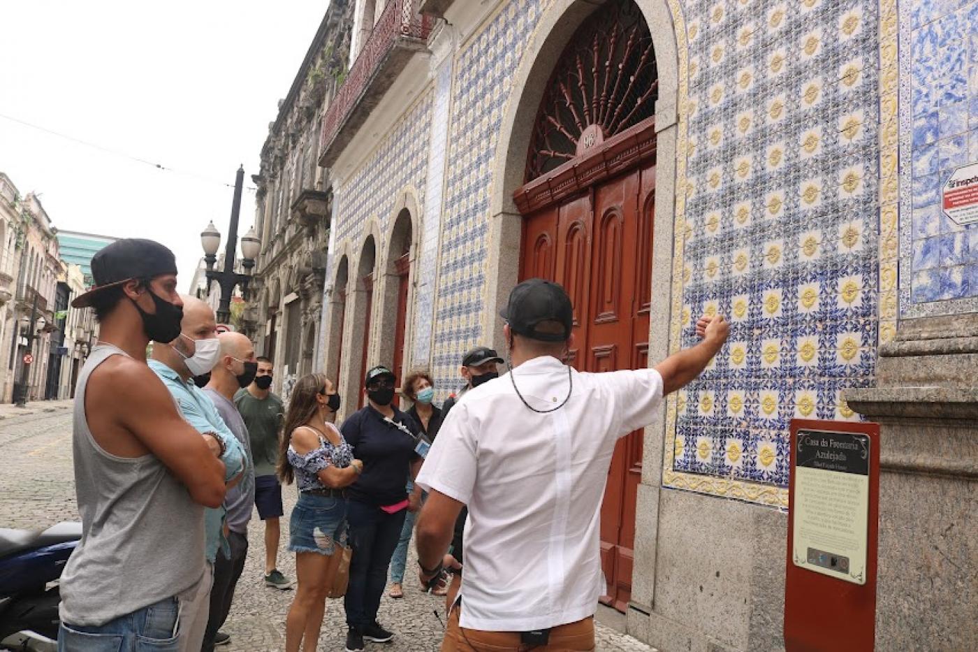 pessoas estão paradas olhando para a fachada da casa da frontaria azulejada. #paratodosverem