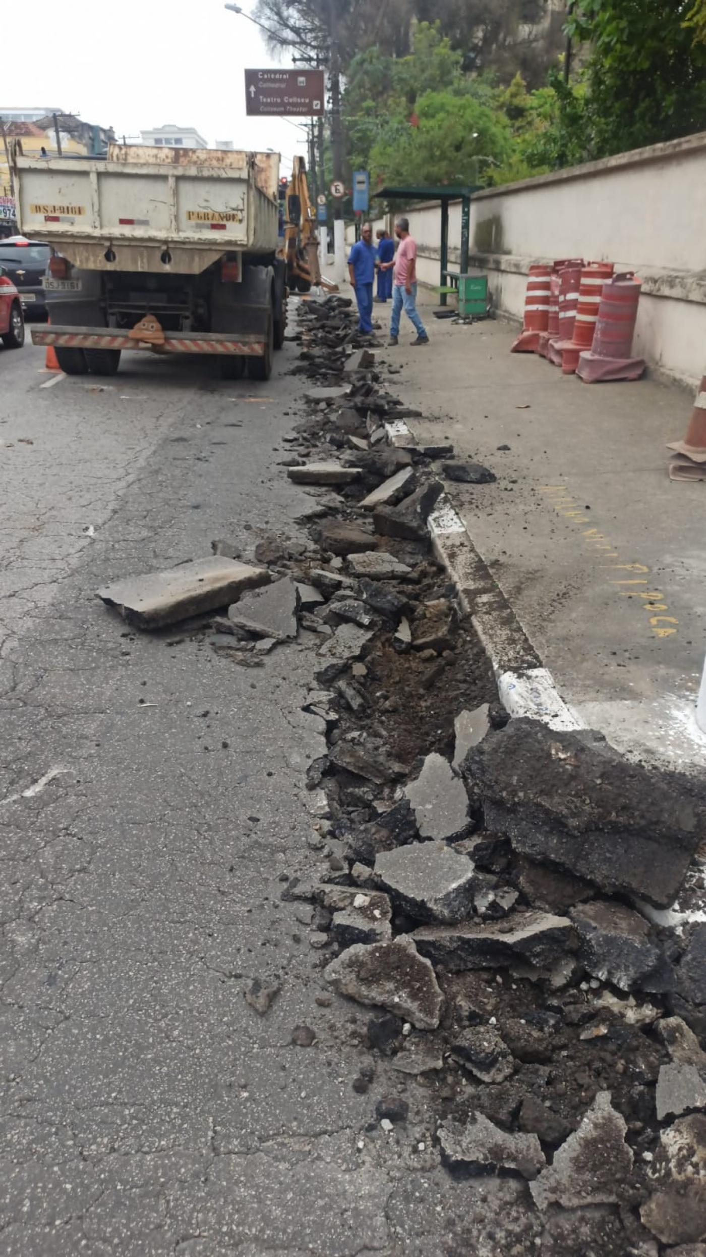 trecho de via com sarjeta quebrada. Ao fundo se vê um ponto de ônibus. #paratodosverem