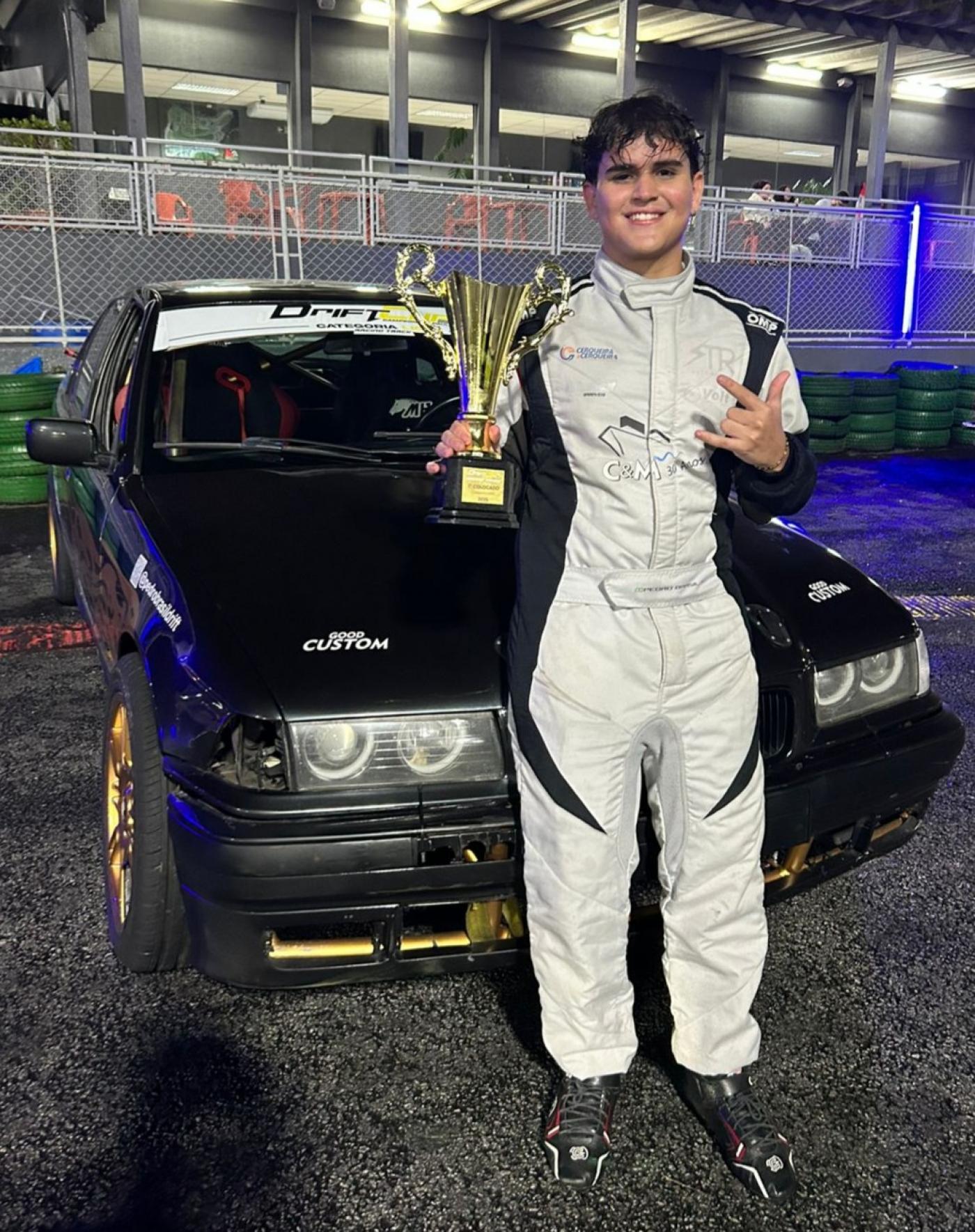 Imagem do piloto com o carro e troféu. #Paratodosverem.