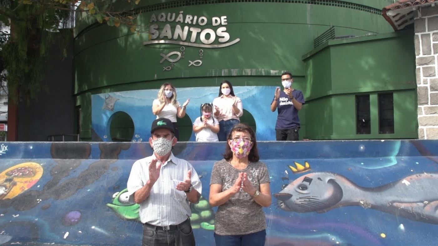 Família está em frente à fachada do Aquário e bate palmas. #Paratodosverem