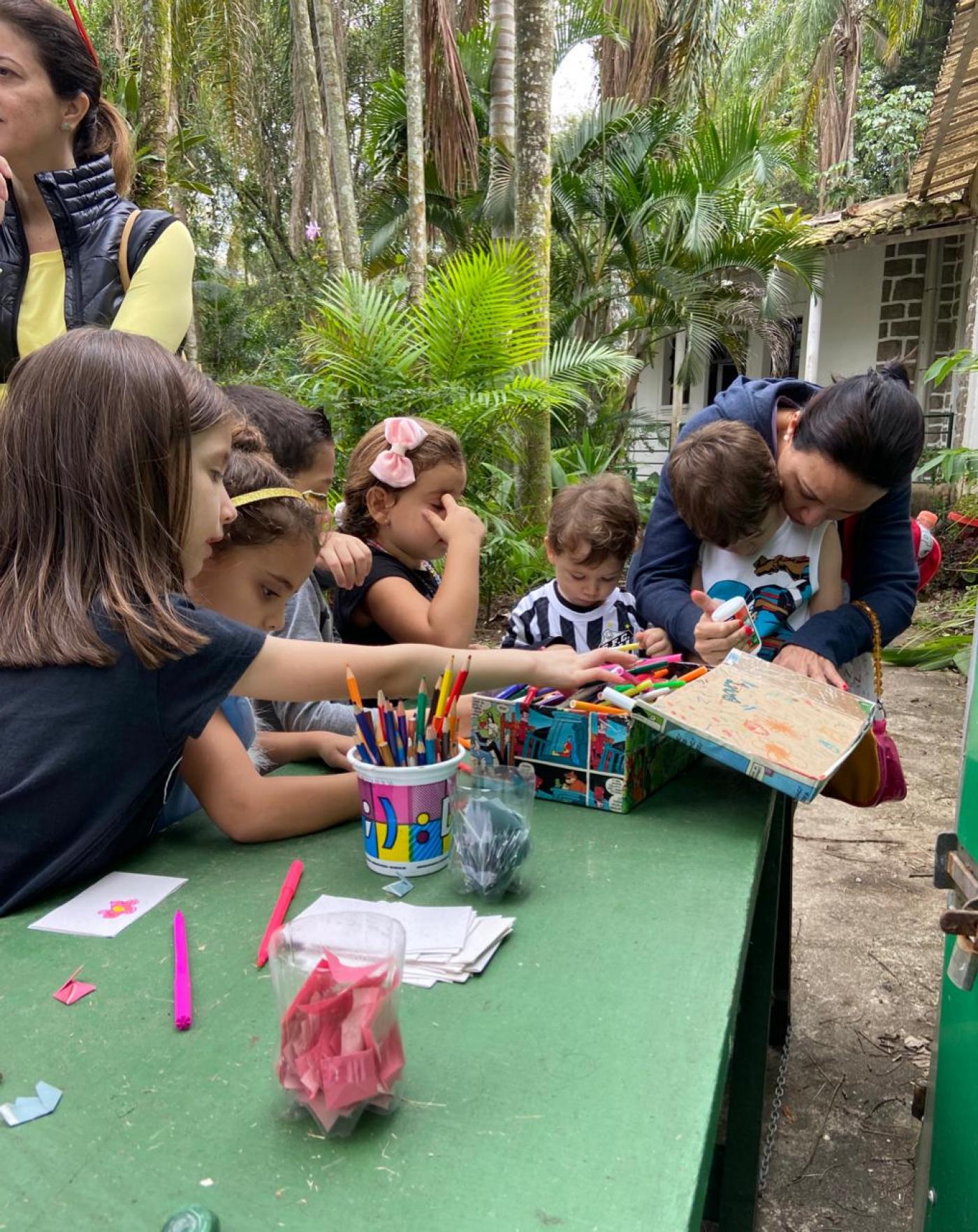 crianças se divertem com dobradura e pintura sobre uma mesa. #paratodosverem