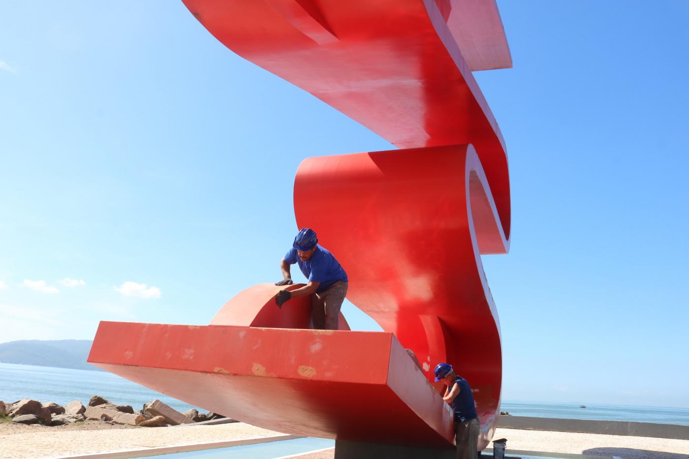 dois homens pintam escultura vermelha. #paratodosverem