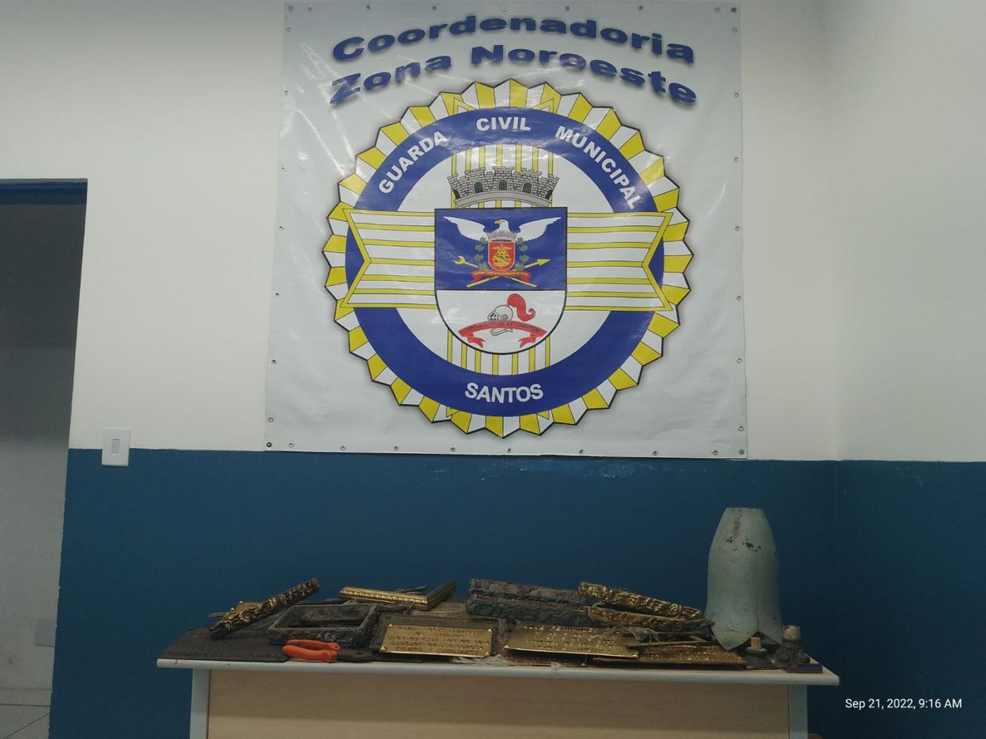 Placas e molduras de bronze retiradas de cemitério sobre mesa em sede da Guarda. #paratodosverem