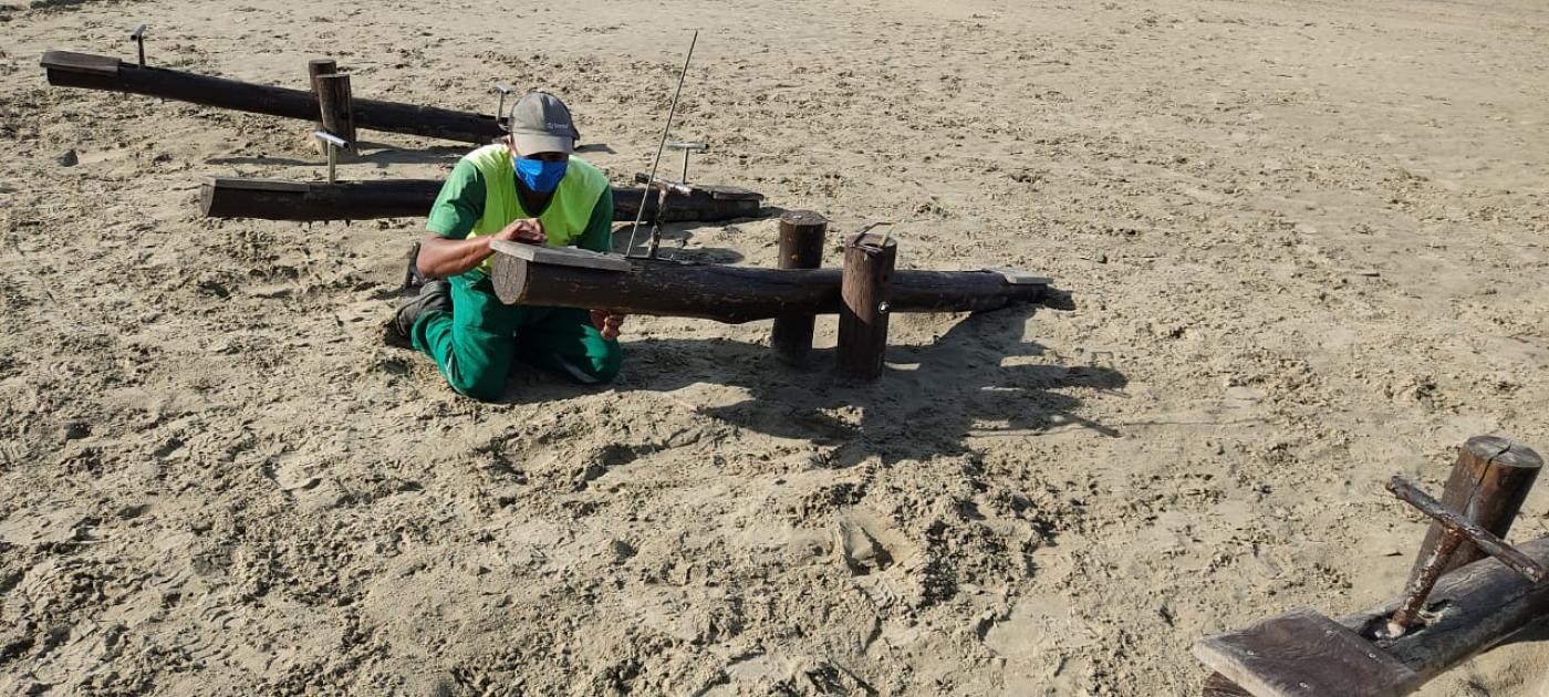 homem trabalha na recuperação de gangorra na areia. #paratodosverem