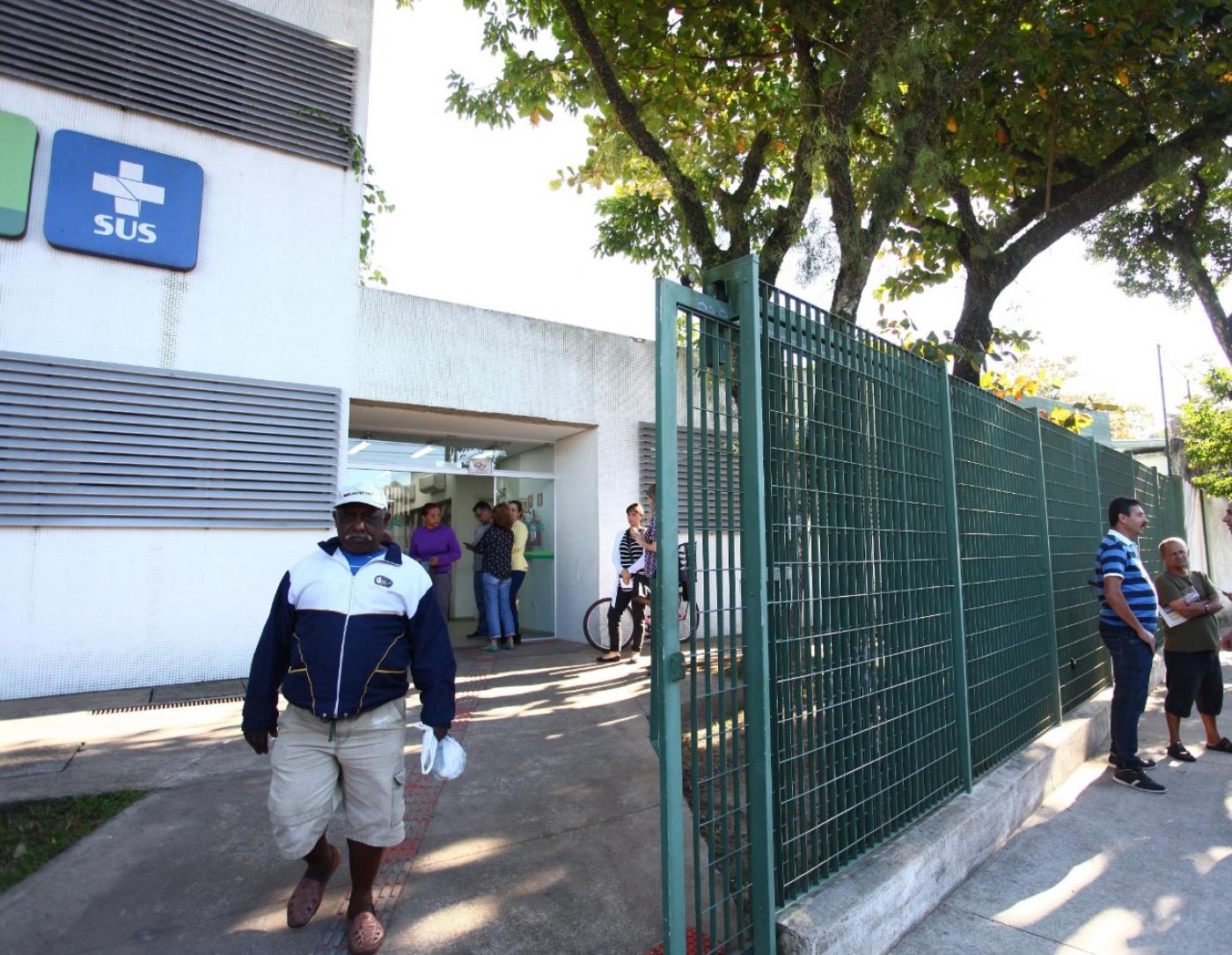 Homem sai da unidade de saúde e passa por portão. #paratodosverem