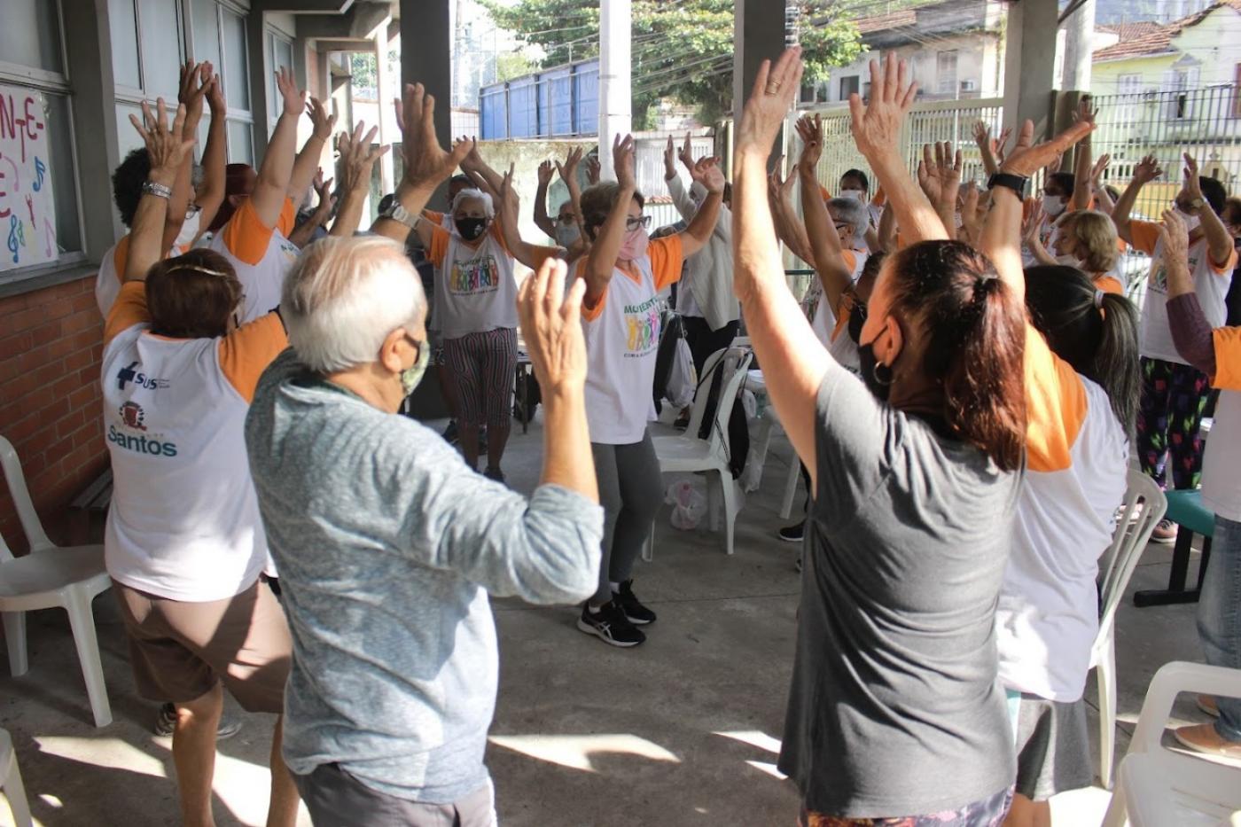 pessoas fazem movimento de alongamento em pé. #paratodosverem
