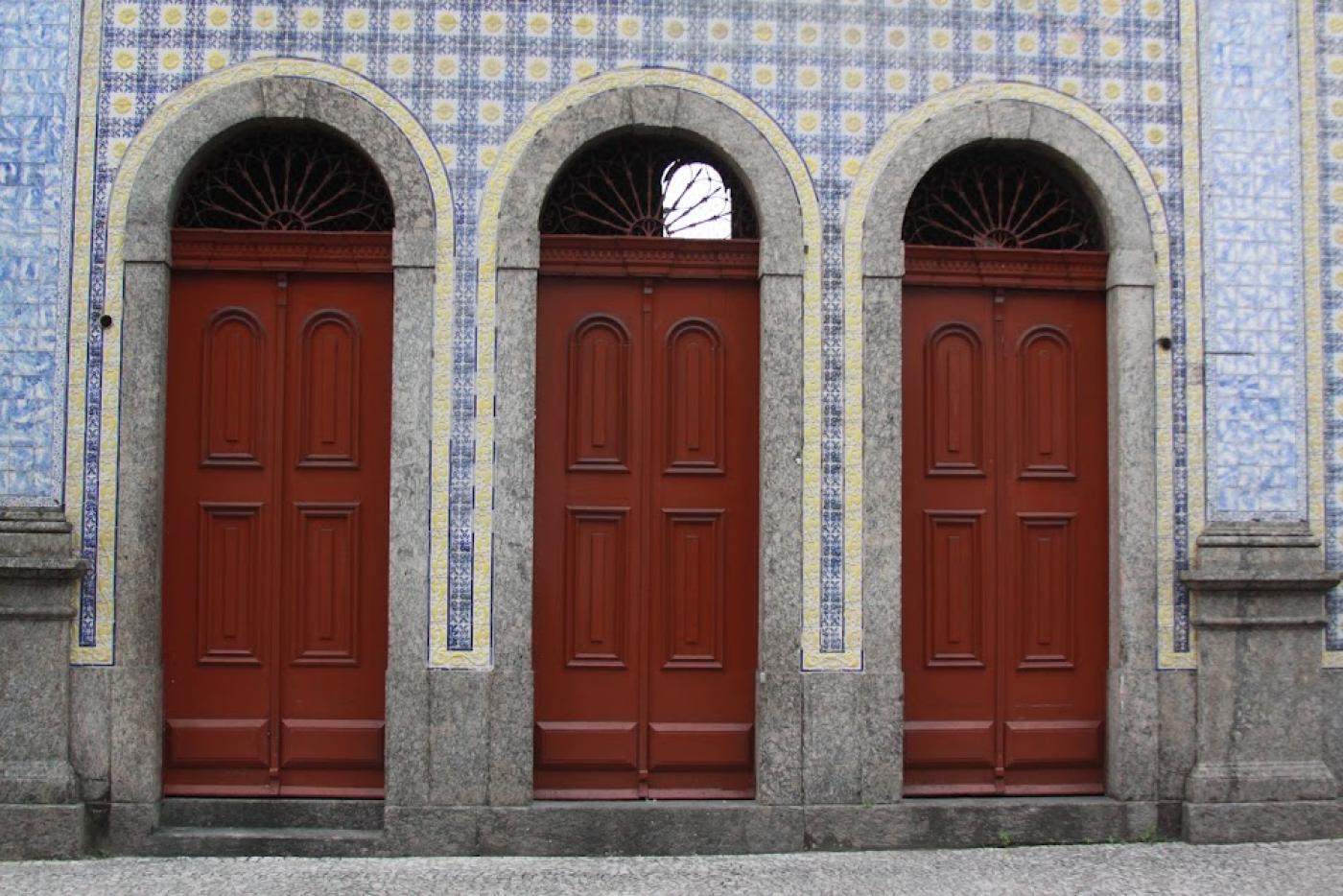 três portas na entrada de uma única edificação azulejada. #paratodosverem