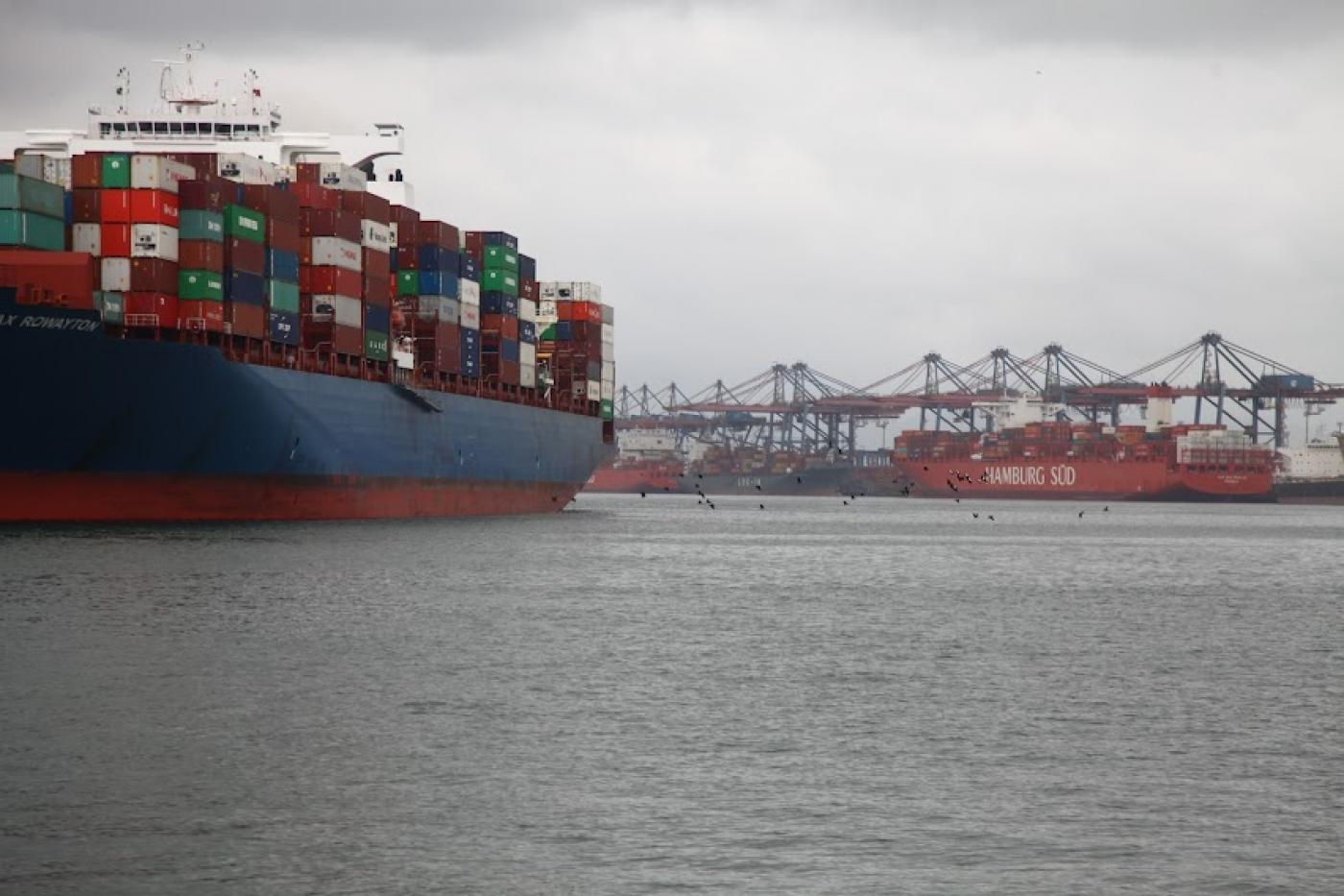 navio navegando e outro ao fundo encostado no cais. Portêineres estão mais ao fundo. #paratodosverem