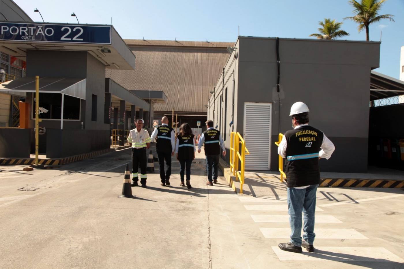 agentes uniformizados e com capacetes estão em frente a um dos portões de entrada de terminal portuário. #paratodosverem