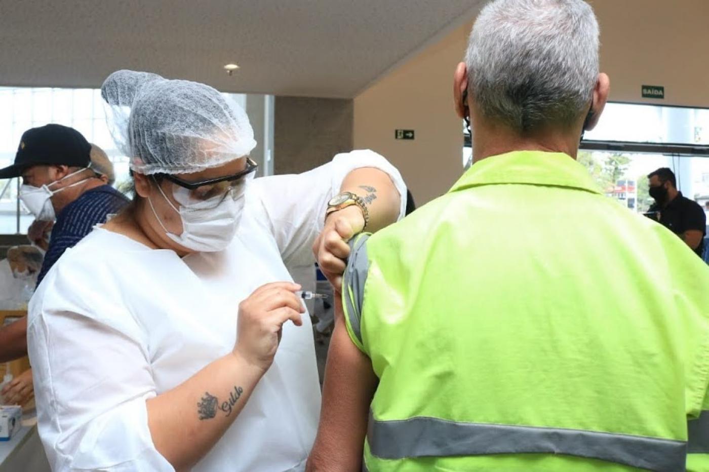 Mulher imuniza portuário. ele usa colete com faixa reflexiva. #paratodosverem