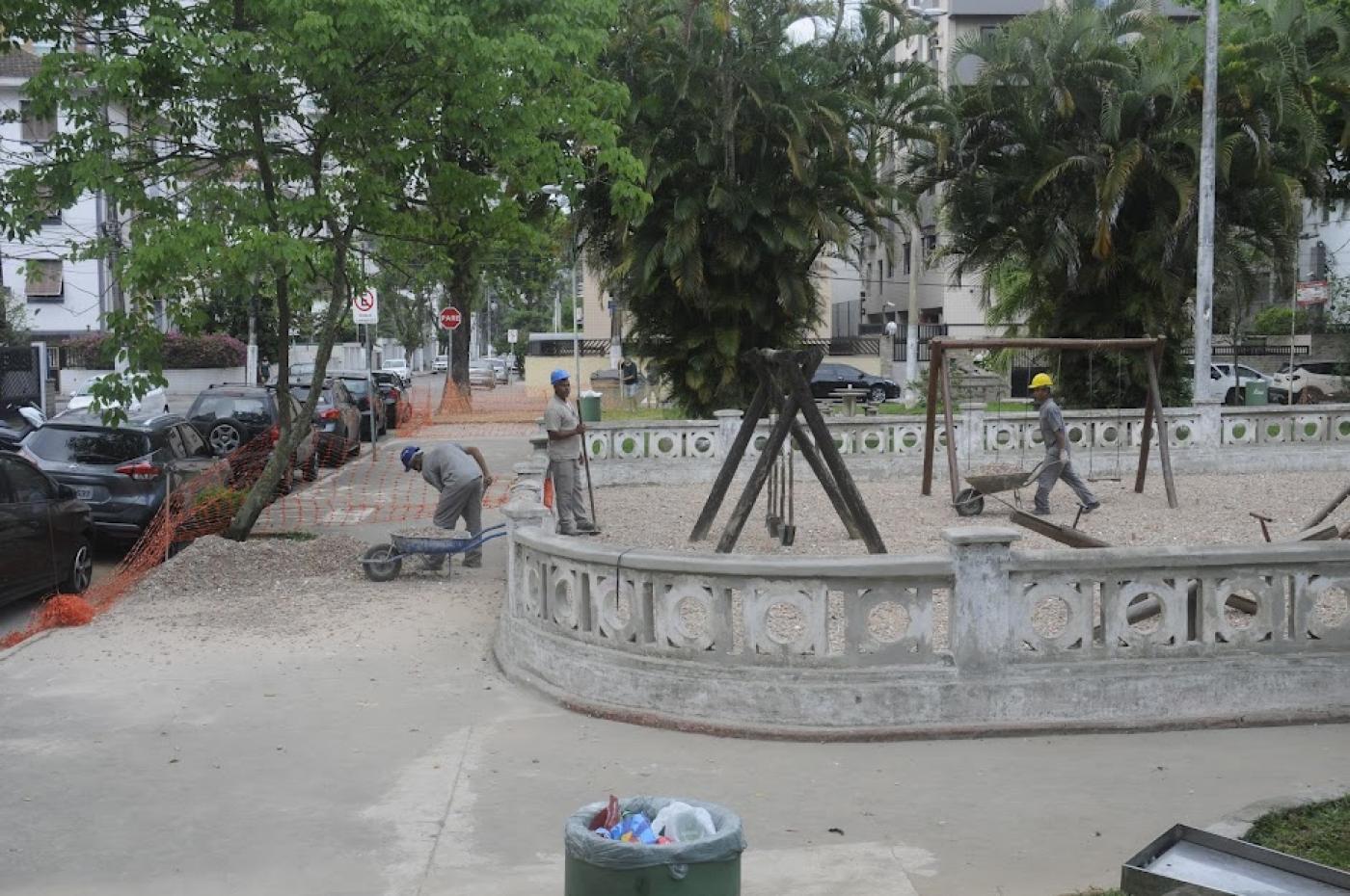 dois homens trabalham na obra de praça. A calçada tem árvores e o entorno da praça tem as tradicionais muretas da Cidade. #paratodosverem