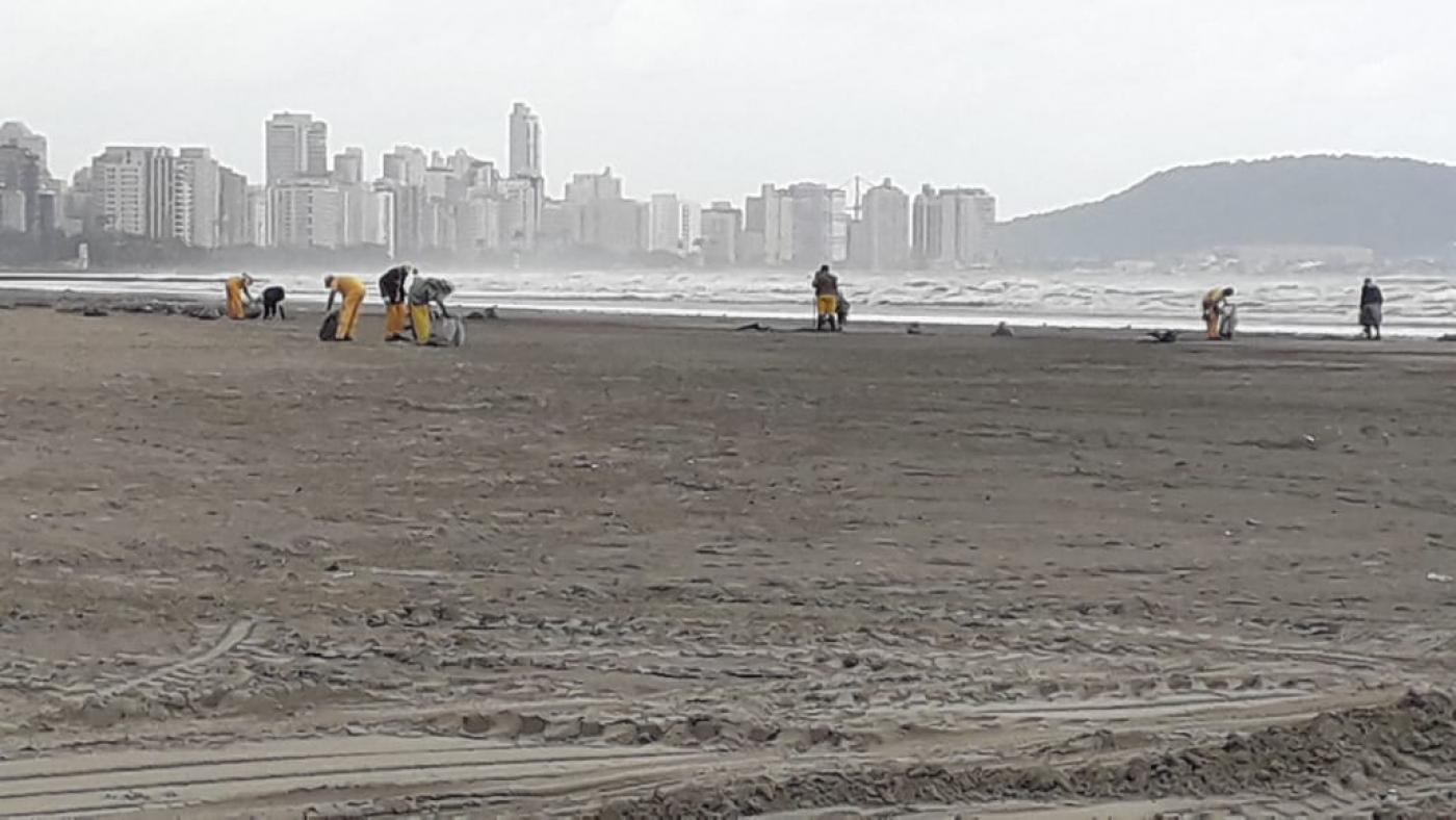 Operários estão recolhendo lixo da faixa de areia em dia nublado. #Paratodosverem