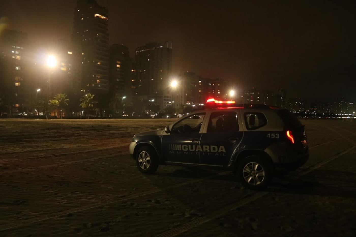 Viatura da GCM na praia e torres de iluminação acesas ao fundo #paratodosverem