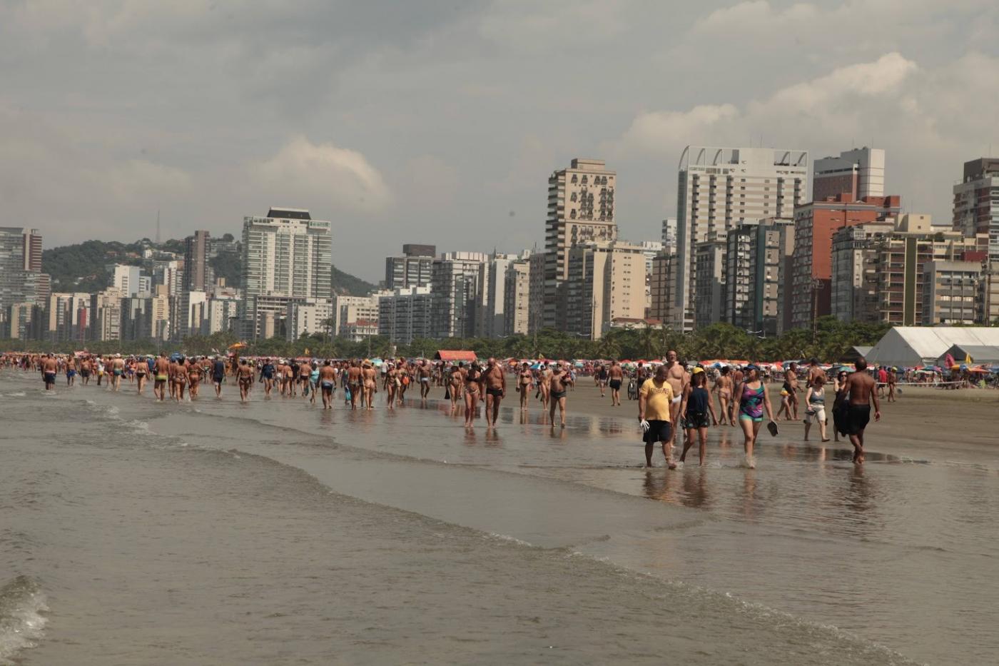pessoas caminhando na praia à beira d'água. #paratodosverem 