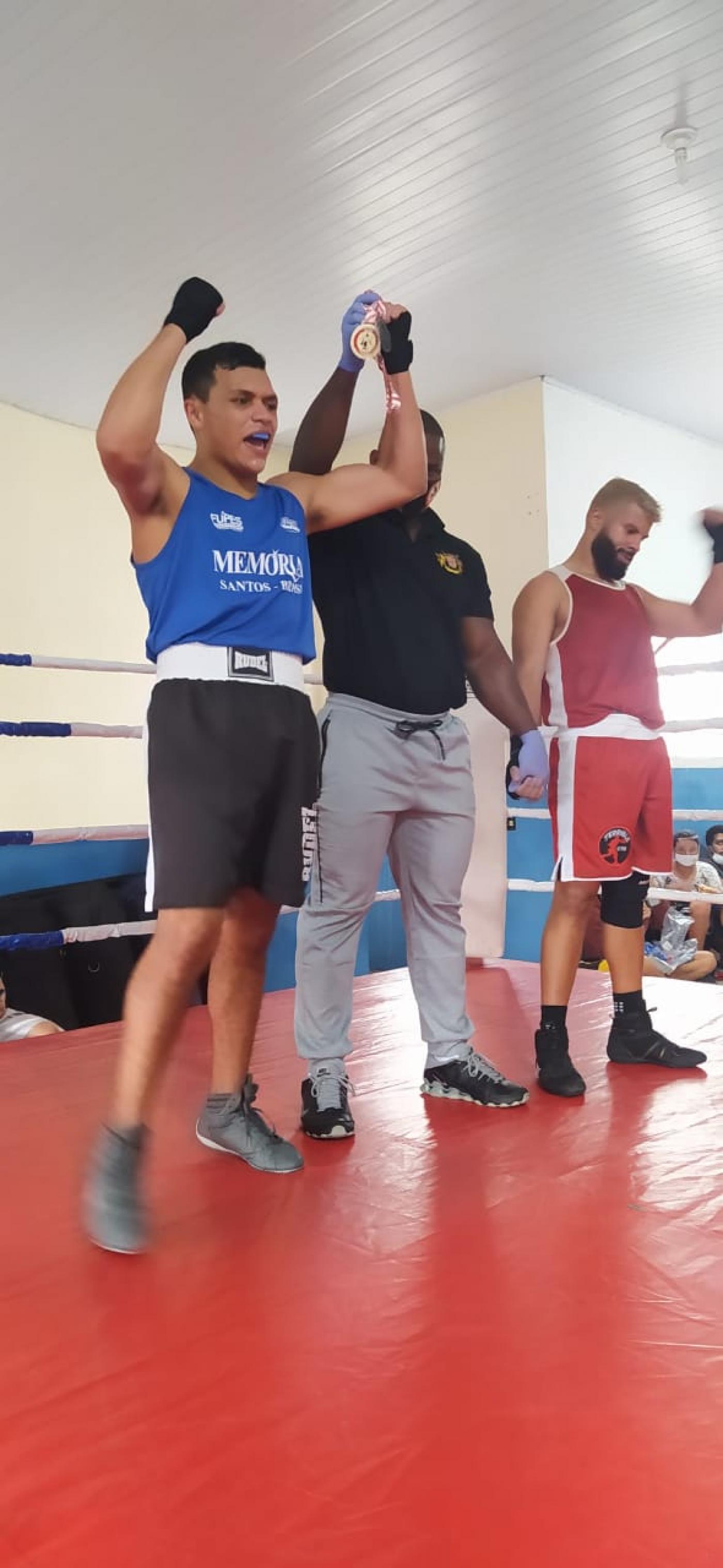 o arbitro, ao centro da foto, ergue os braços de dois pugilistas. O da esquerda, usando camisa azul, é Lucas Vinícius. #paratodosverem