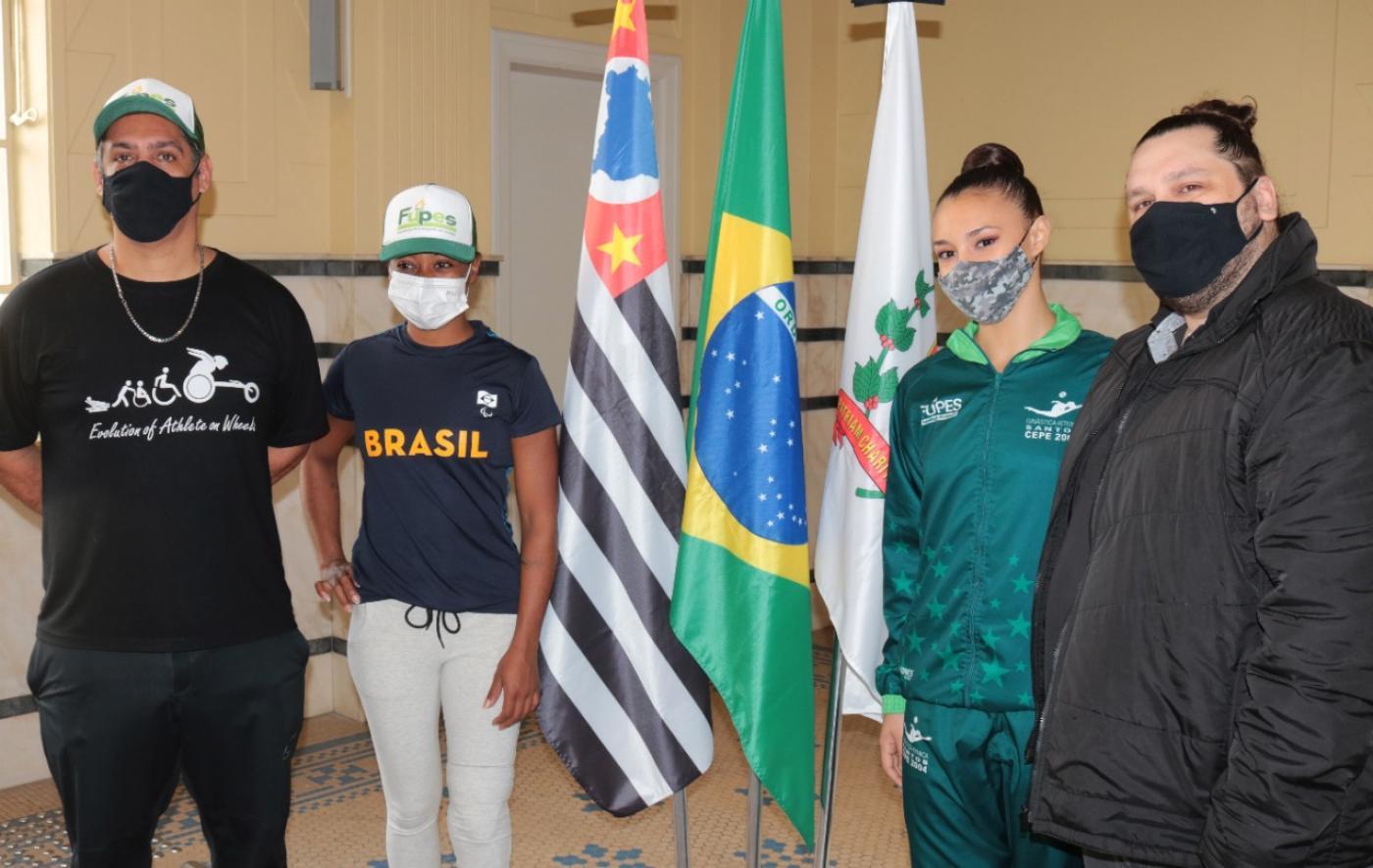 Eduardo Leonel e Vanessa Souza e Sarah Nascimento com sei treinador. Eles ladeiam as bandeiras de SP, Brasil e Santos. #paratodosverem