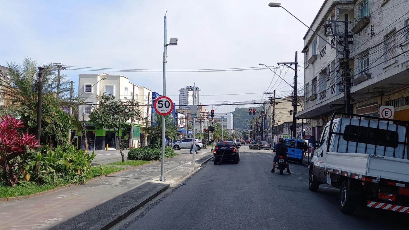 via com caminhonete estacionada à direita. Placa indicando velocidade máxima e radar no alto do poste. #paratodosverem