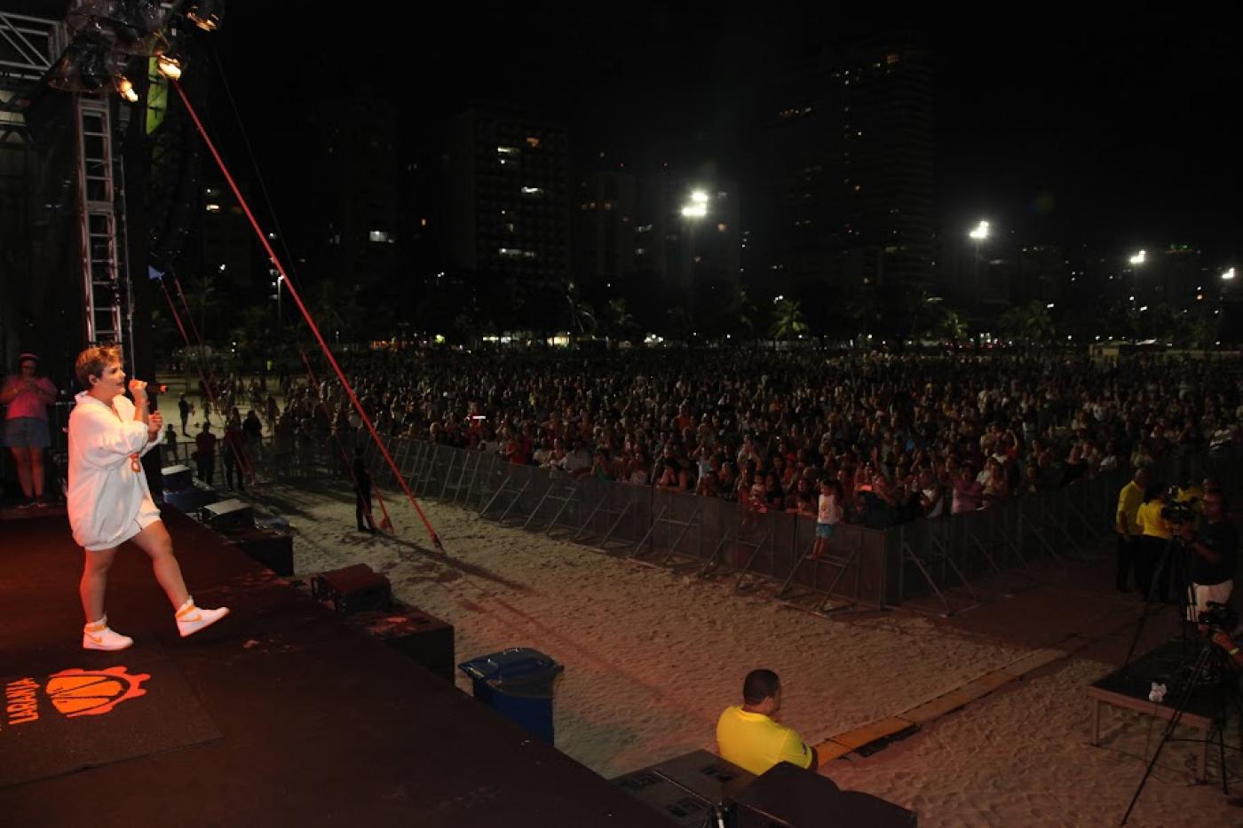Cantora no palco e público ao fundo na Praia do Gonzaga. #pratodosverem