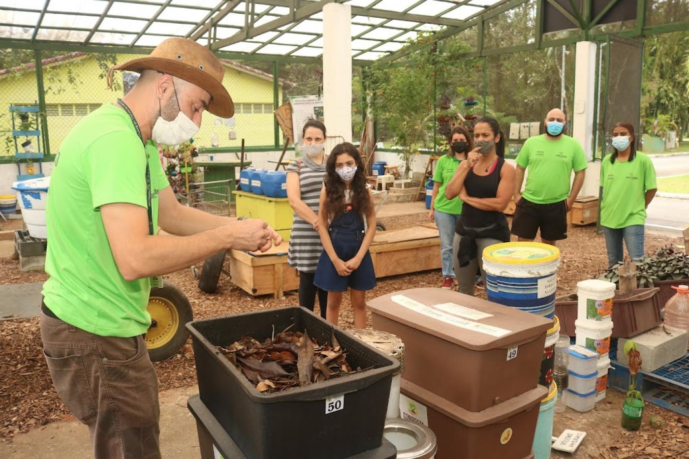 pessoa ensina técnica de compostagem e outras observam em centro #paratodosverem