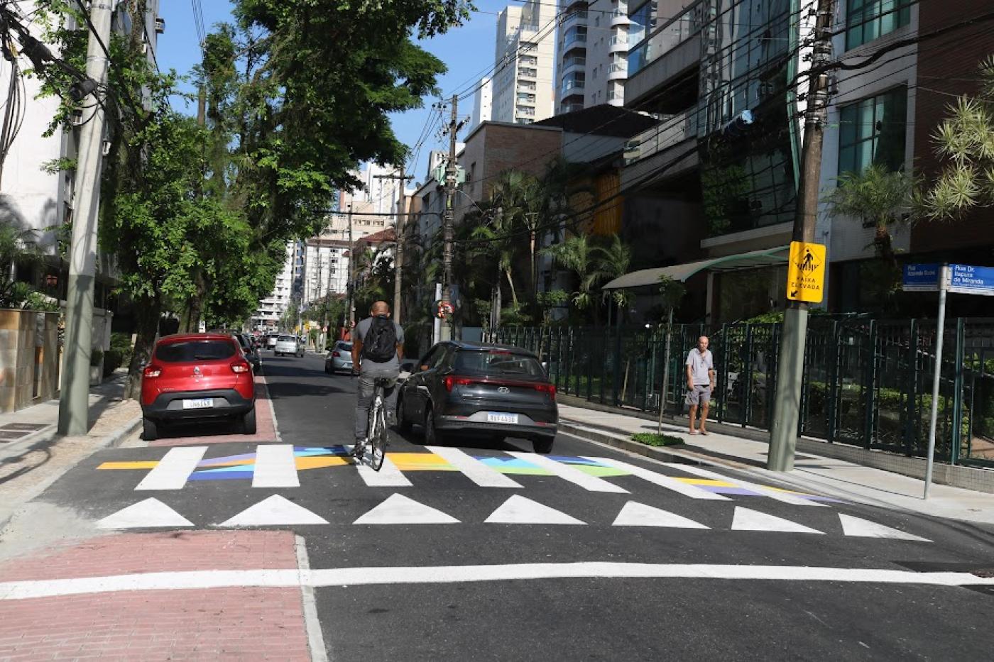 ciclista e carro passam sobre faixa de pedestre estilizada. #paratodosverem 