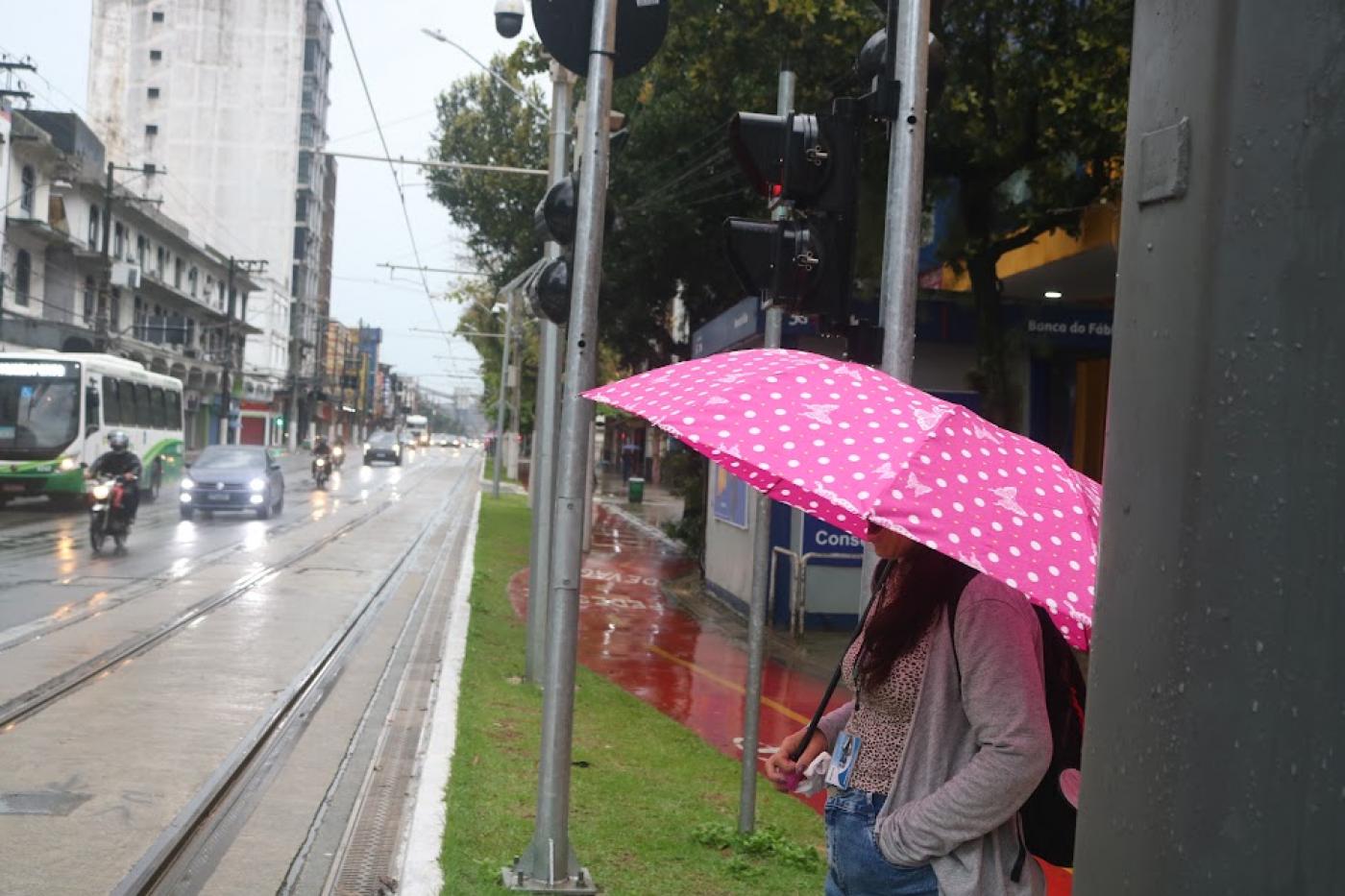 mulher de guarda-chuva espera para atravessar avenida. #paratodosverem