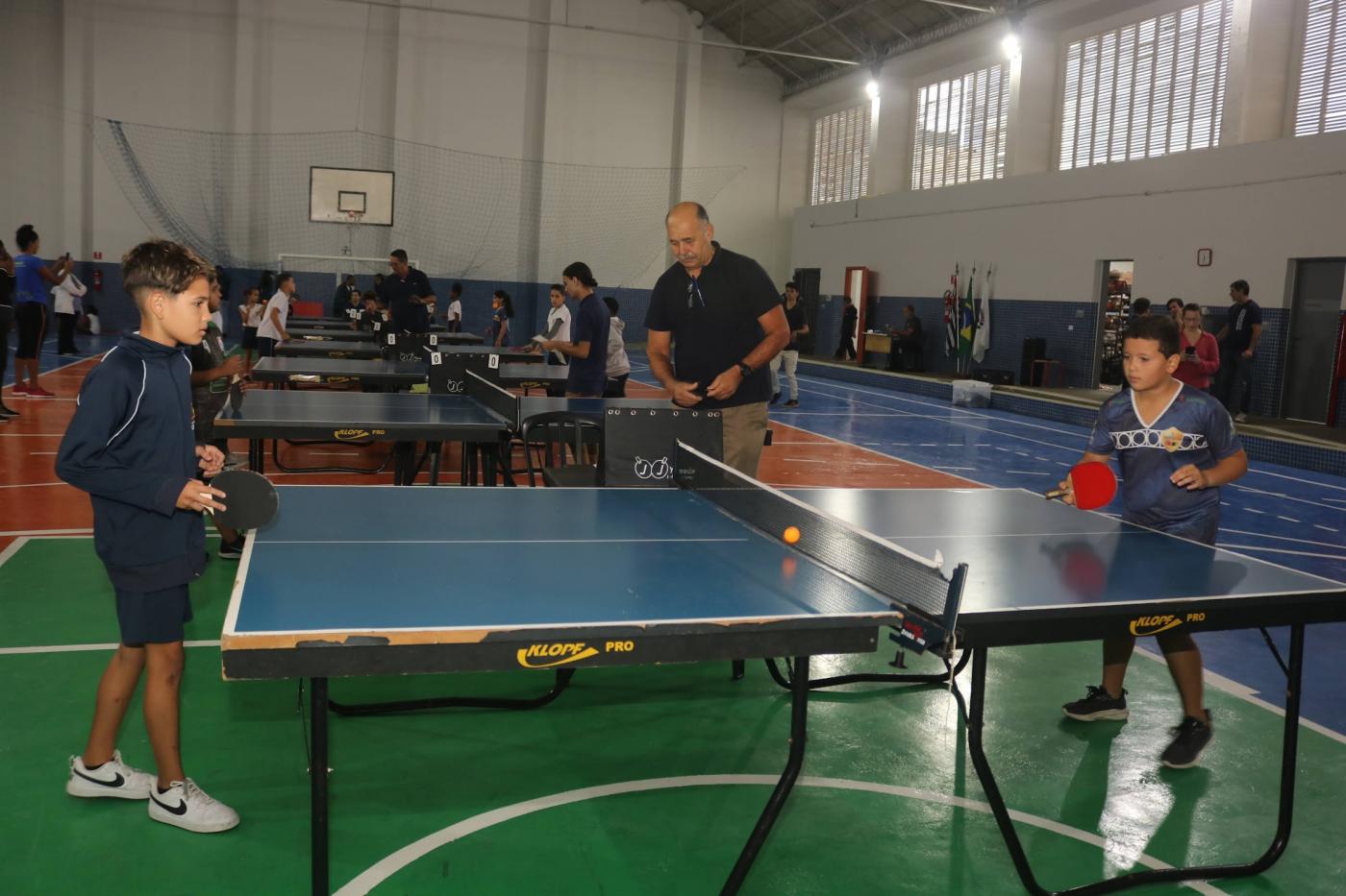 crinças jogam tênis de mesa em quadra. #paratodosverem