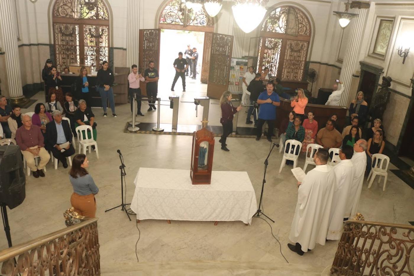 imagem está sobreuma mesa no centro do saguão da prefeitura. Várias pessoas em torno. #paratodosverem 