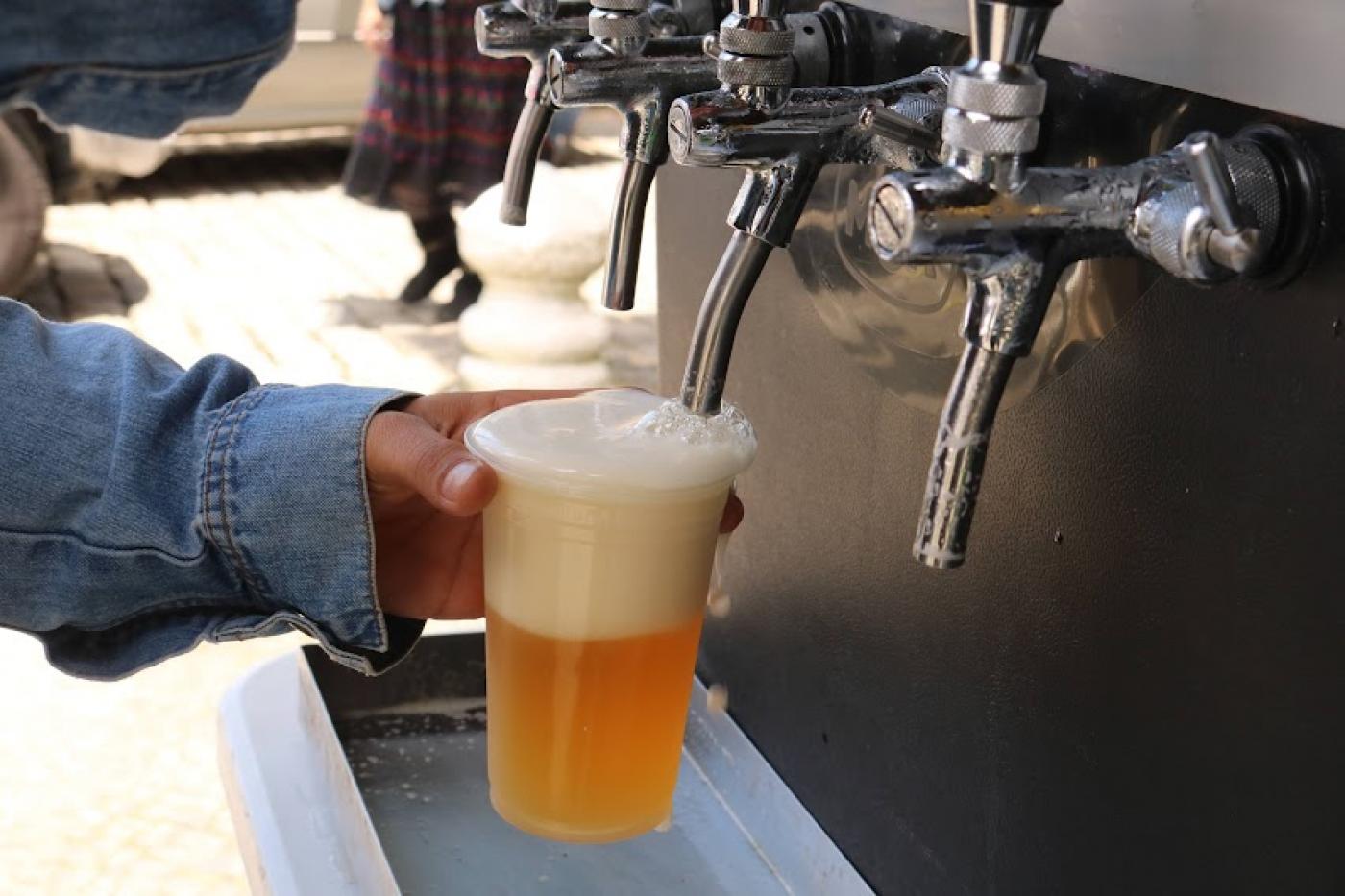 mão segura copo cheio de cerveja encostado no bico de uma chopeira. #paratodosverem