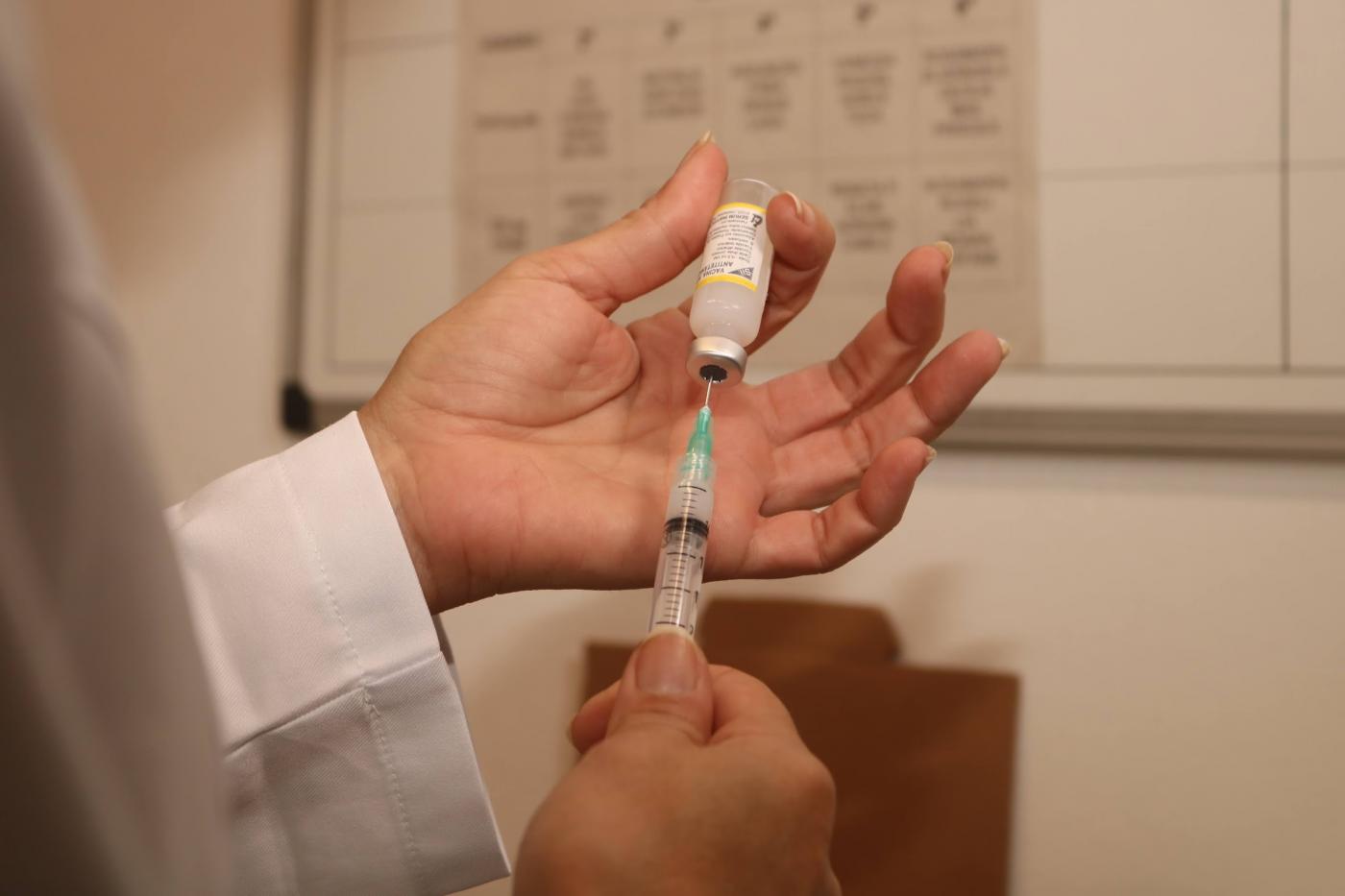 mãos seguram frasco de vacina e agulha com seringa. #paratodosverem