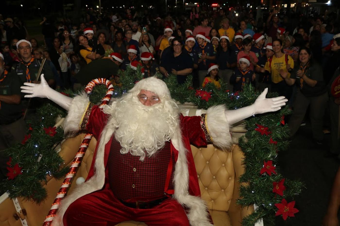 papai noel de braços abertos com grande público ao fundo. #paratodosverem